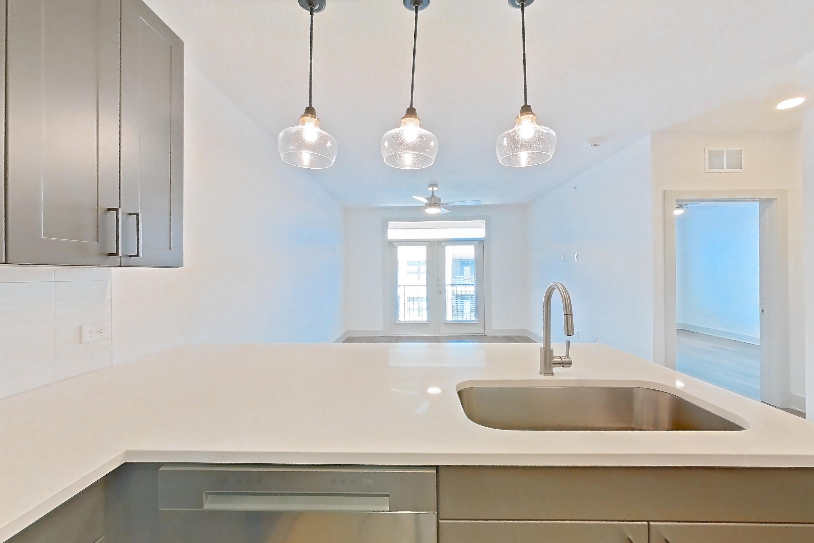 Kitchen with dishwasher, electric range, light countertops, light stone countertops, light wood-finish flooring, microwave, oven/range, and stainless steel appliances, Apartment 2405 at Groves South Congress