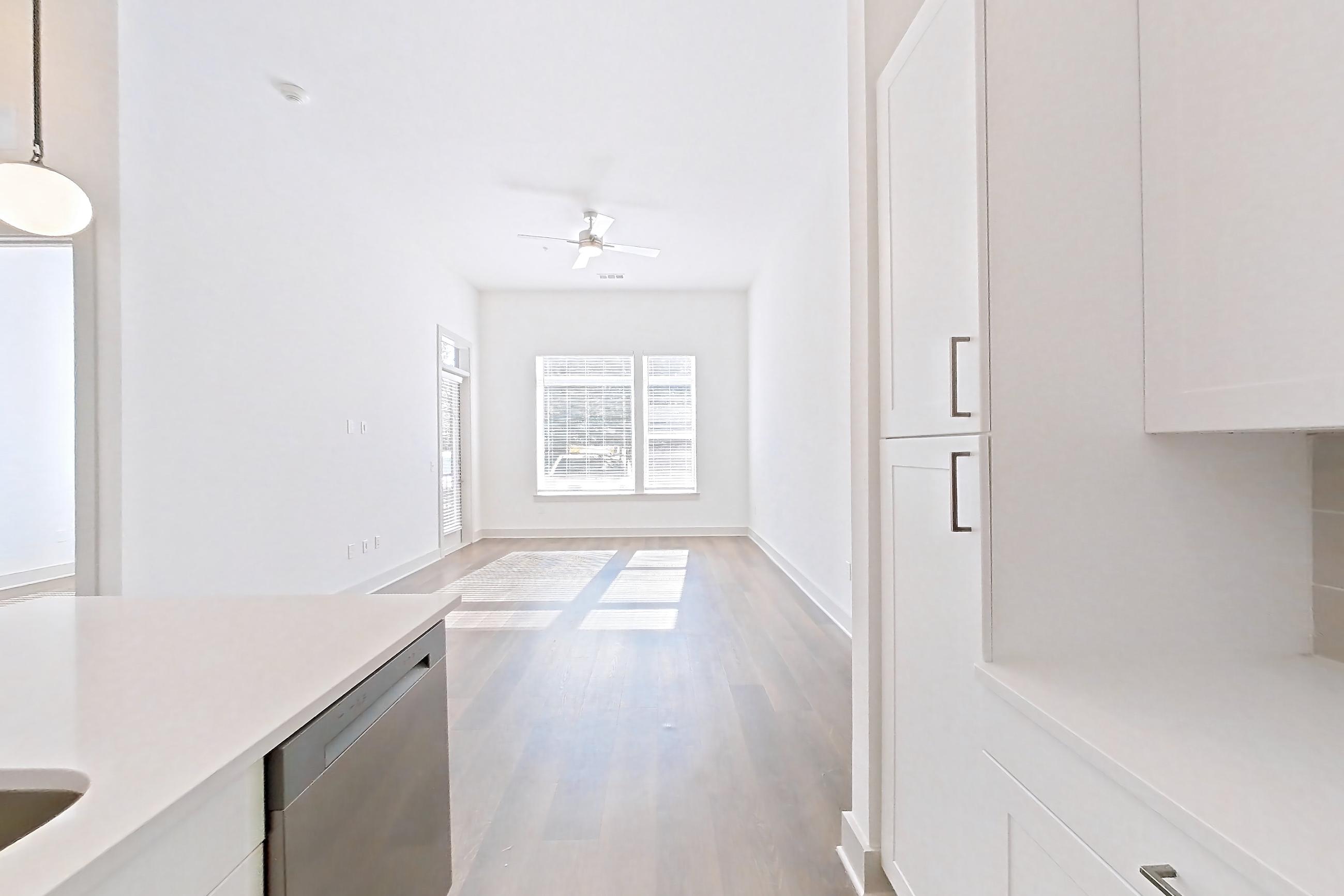 Kitchen with dark wood-finish flooring, dishwasher, electric range, kitchen island, light countertops, light stone countertops, light wood-finish flooring, microwave, oven/range, and stainless steel appliances, Apartment 2148 at Groves South Congress