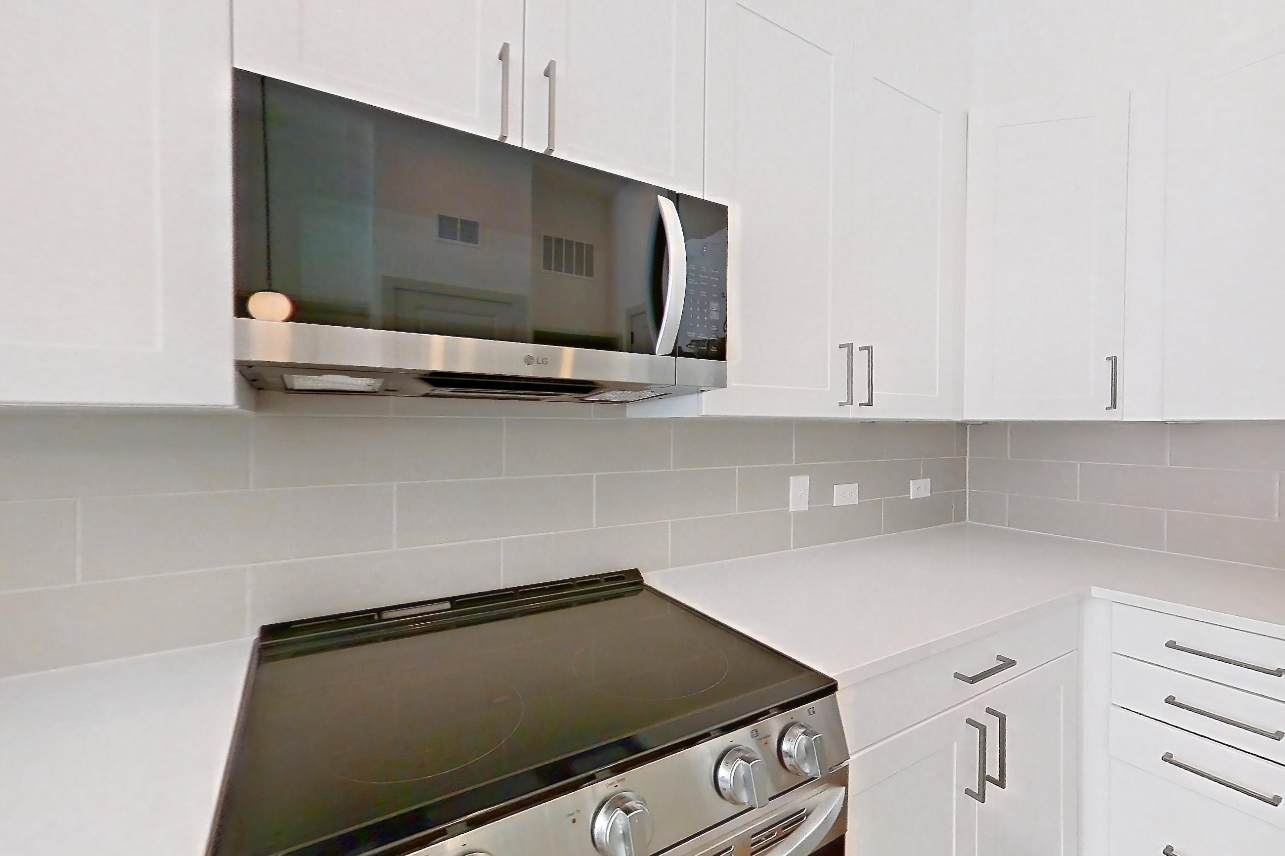 Kitchen with dark wood-finish flooring, dishwasher, electric range, kitchen island, light countertops, light stone countertops, light wood-finish flooring, microwave, oven/range, and stainless steel appliances, Apartment 2148 at Groves South Congress