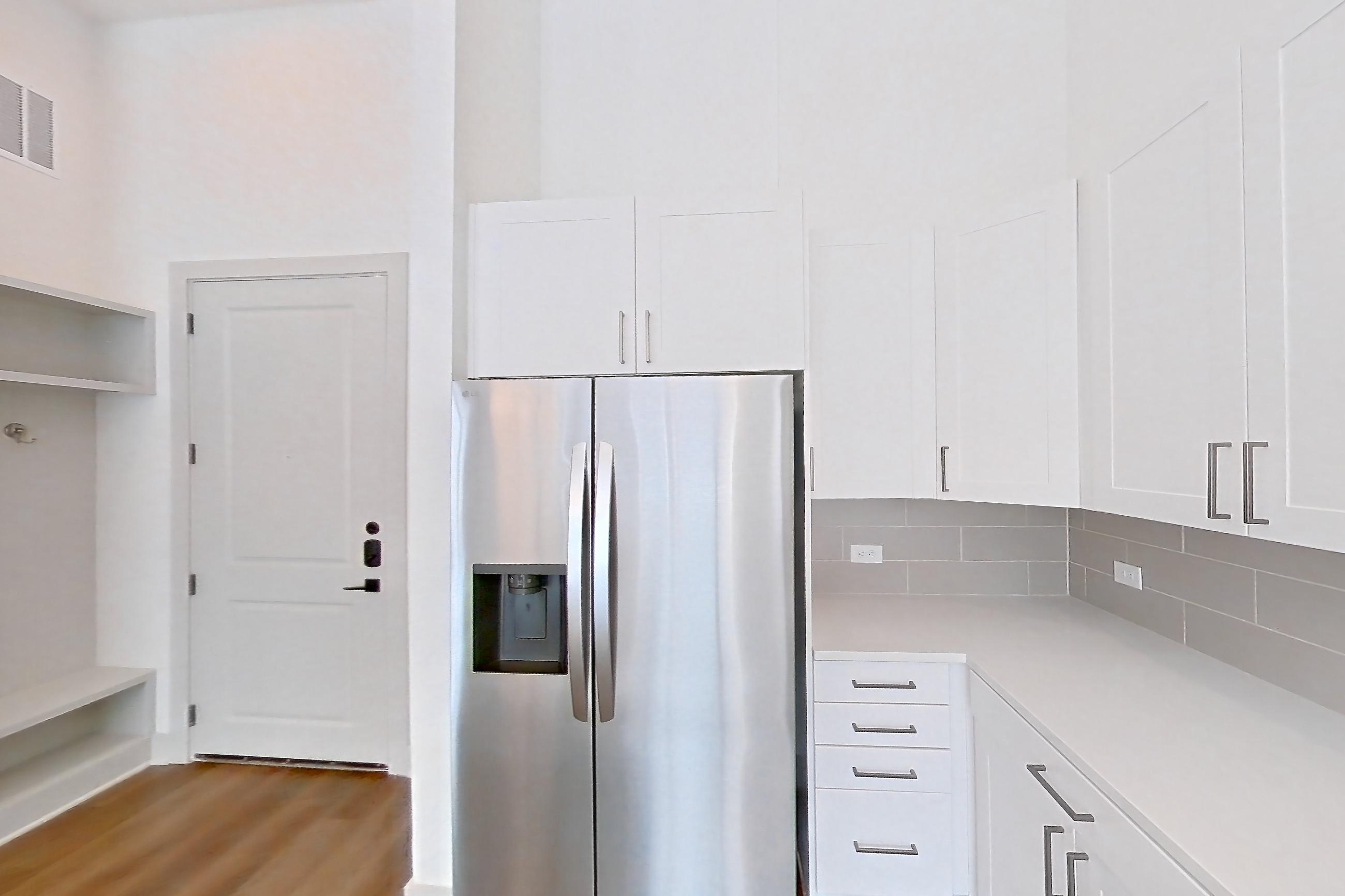 Kitchen with electric range, light countertops, light wood-finish flooring, oven/range, refrigerator, stainless steel appliances, and water & ice dispenser, Apartment 2149 at Groves South Congress