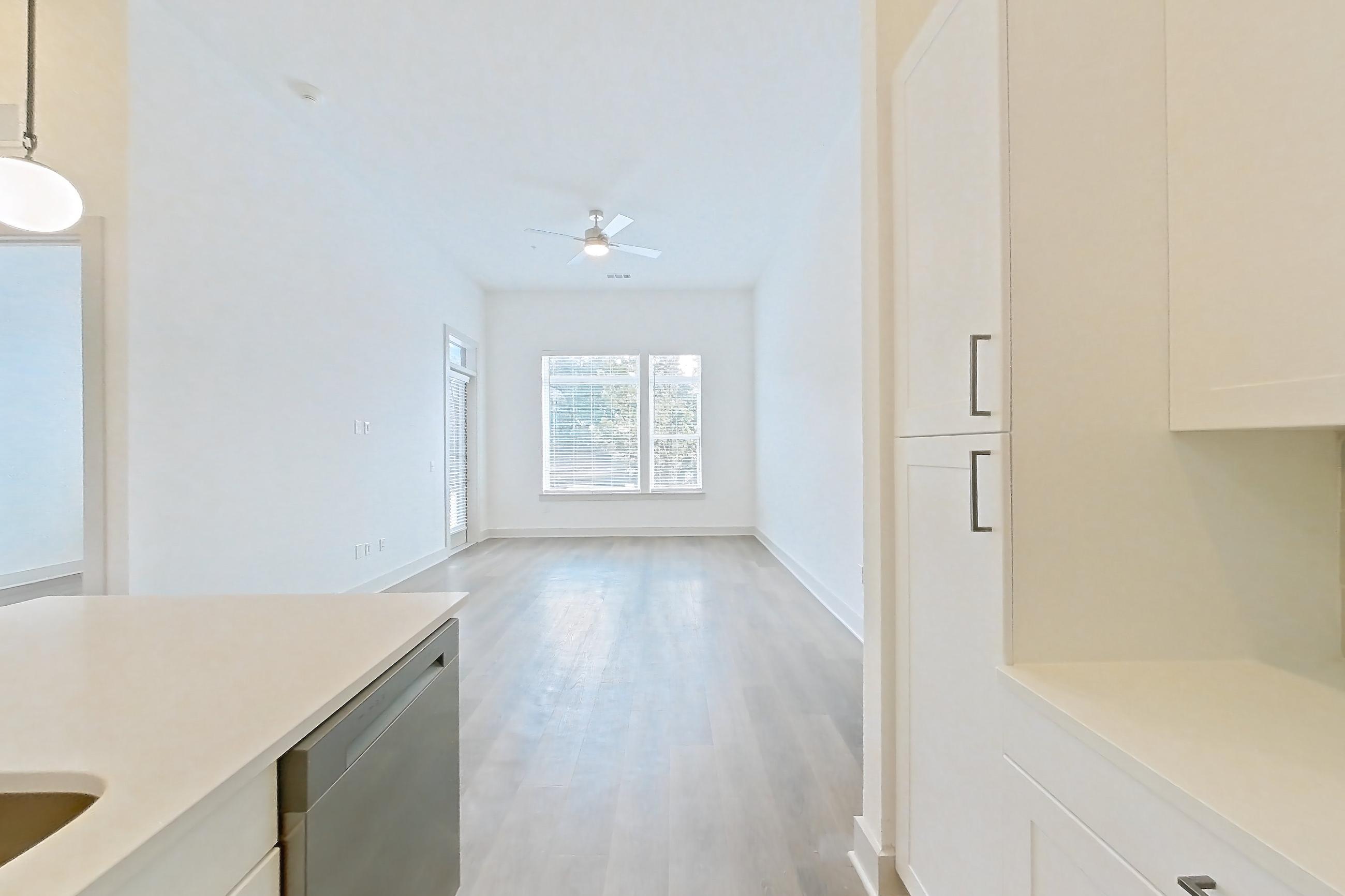 Kitchen with dark wood-finish flooring, dishwasher, electric range, kitchen island, light countertops, light stone countertops, microwave, oven/range, and stainless steel appliances, Apartment 2151 at Groves South Congress