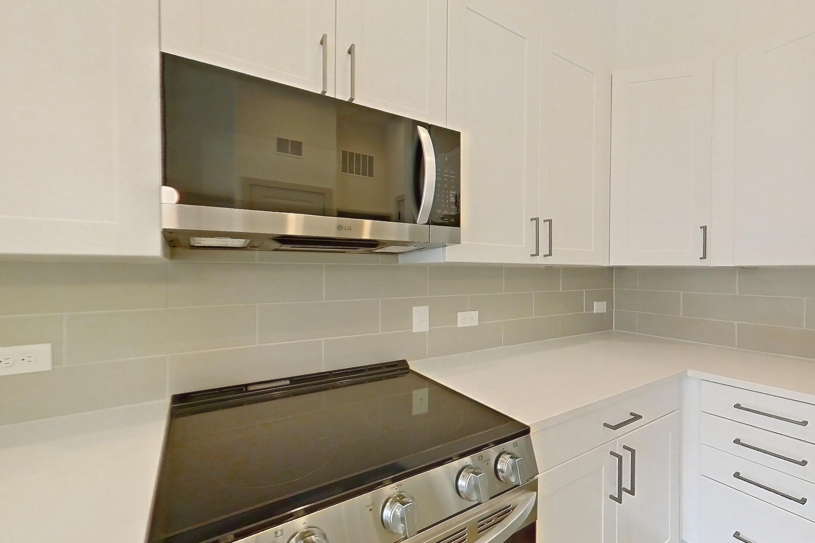 Kitchen with dark wood-finish flooring, dishwasher, electric range, kitchen island, light countertops, light stone countertops, microwave, oven/range, and stainless steel appliances, Apartment 2151 at Groves South Congress