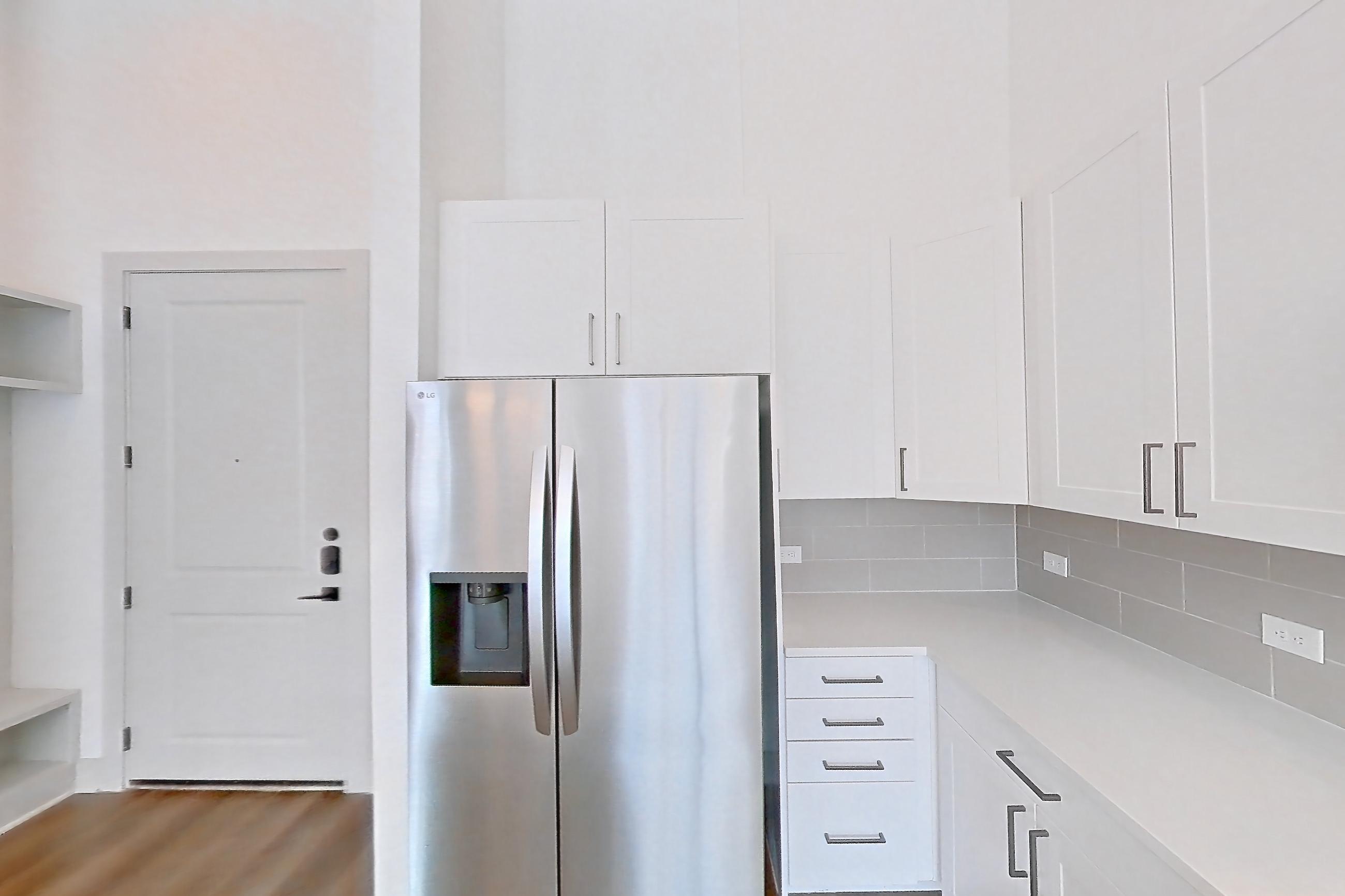 Kitchen with electric range, light countertops, light wood-finish flooring, oven/range, refrigerator, stainless steel appliances, and water & ice dispenser, Apartment 2153 at Groves South Congress
