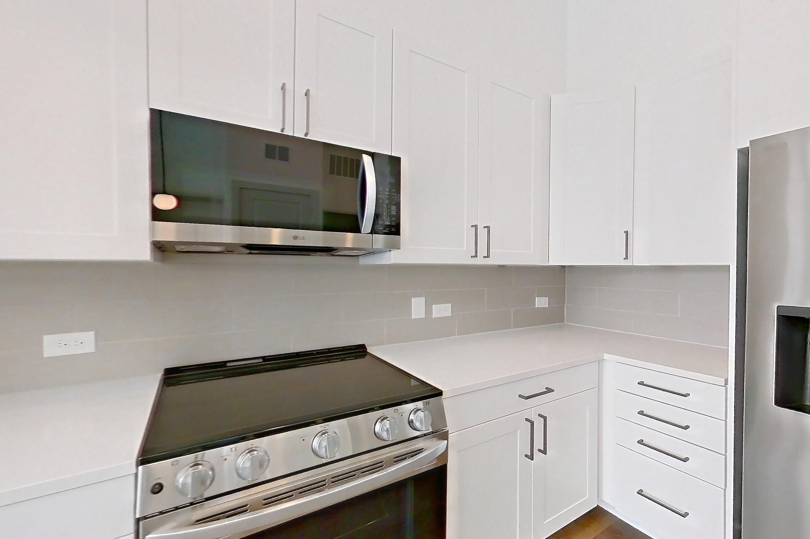 Kitchen with dark wood-finish flooring, dishwasher, electric range, light countertops, light stone countertops, microwave, oven/range, and stainless steel appliances, Apartment 2155 at Groves South Congress