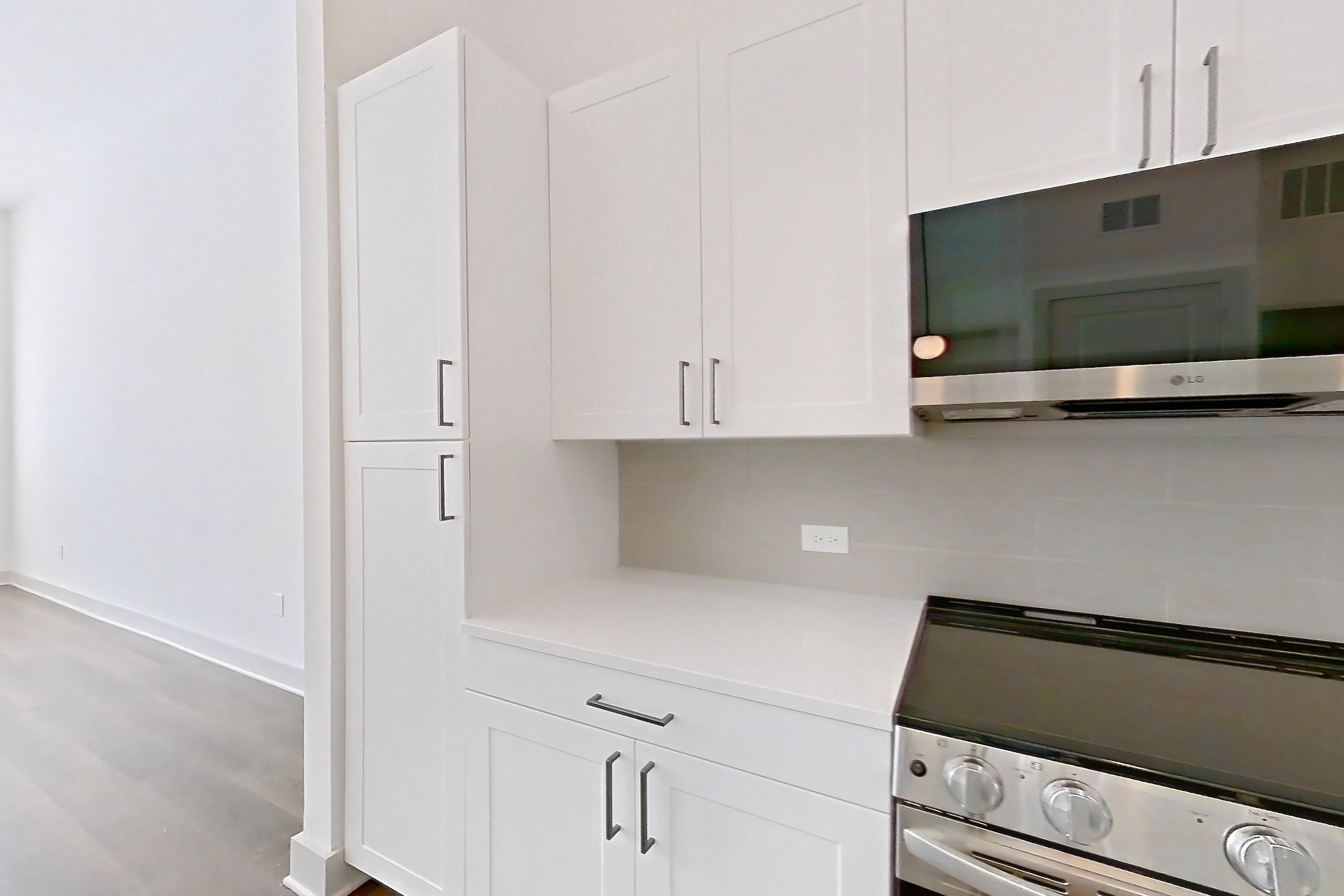 Kitchen with dark wood-finish flooring, dishwasher, electric range, light countertops, light stone countertops, microwave, oven/range, and stainless steel appliances, Apartment 2155 at Groves South Congress