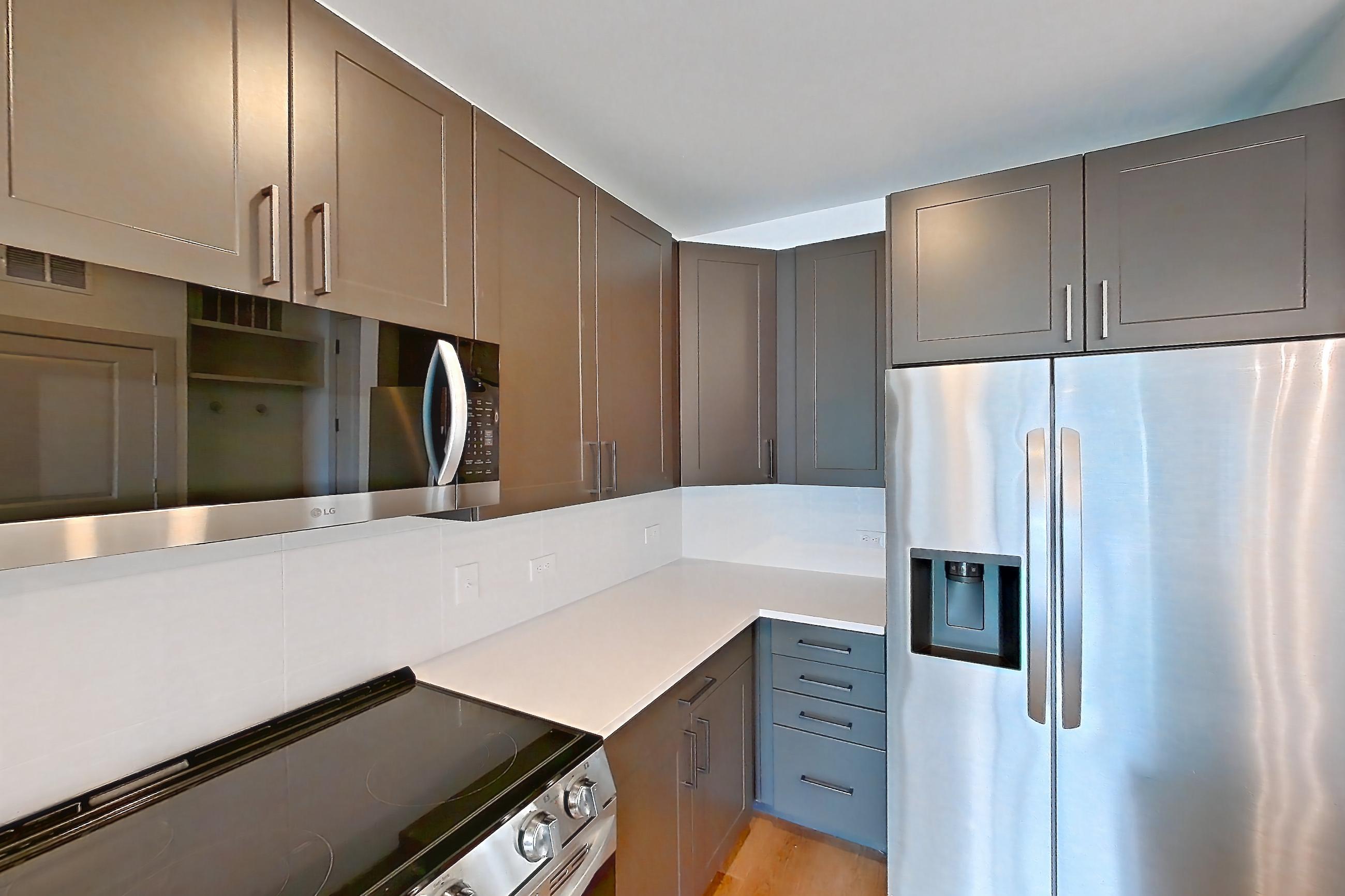 Kitchen with dark wood-finish flooring, electric range, light countertops, light stone countertops, light wood-finish flooring, microwave, oven/range, refrigerator, stainless steel appliances, and water & ice dispenser, Apartment 2251 at Groves South Congress