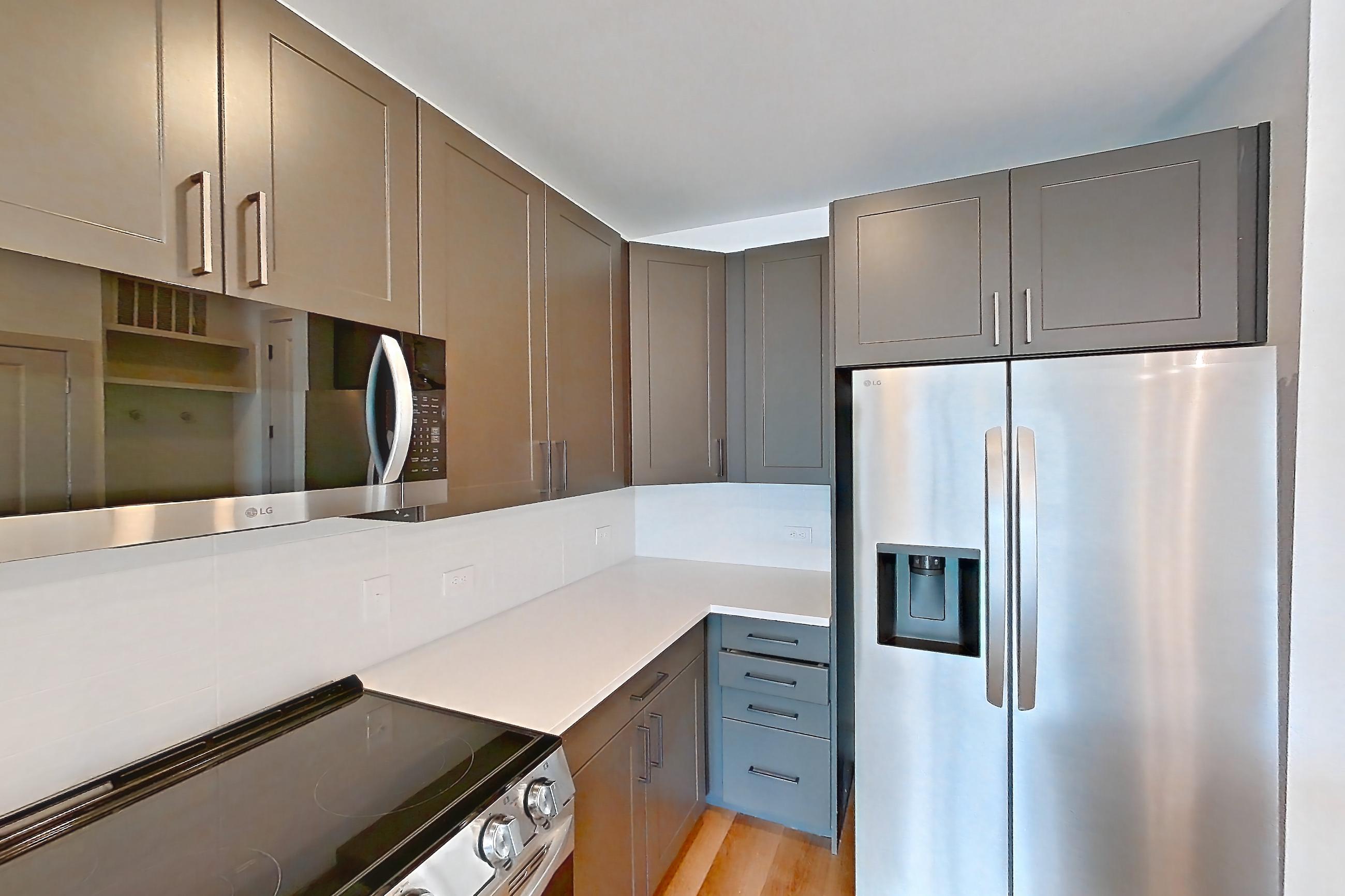 Kitchen with electric range, light countertops, light stone countertops, light wood-finish flooring, microwave, oven/range, refrigerator, stainless steel appliances, and water & ice dispenser, Apartment 2255 at Groves South Congress