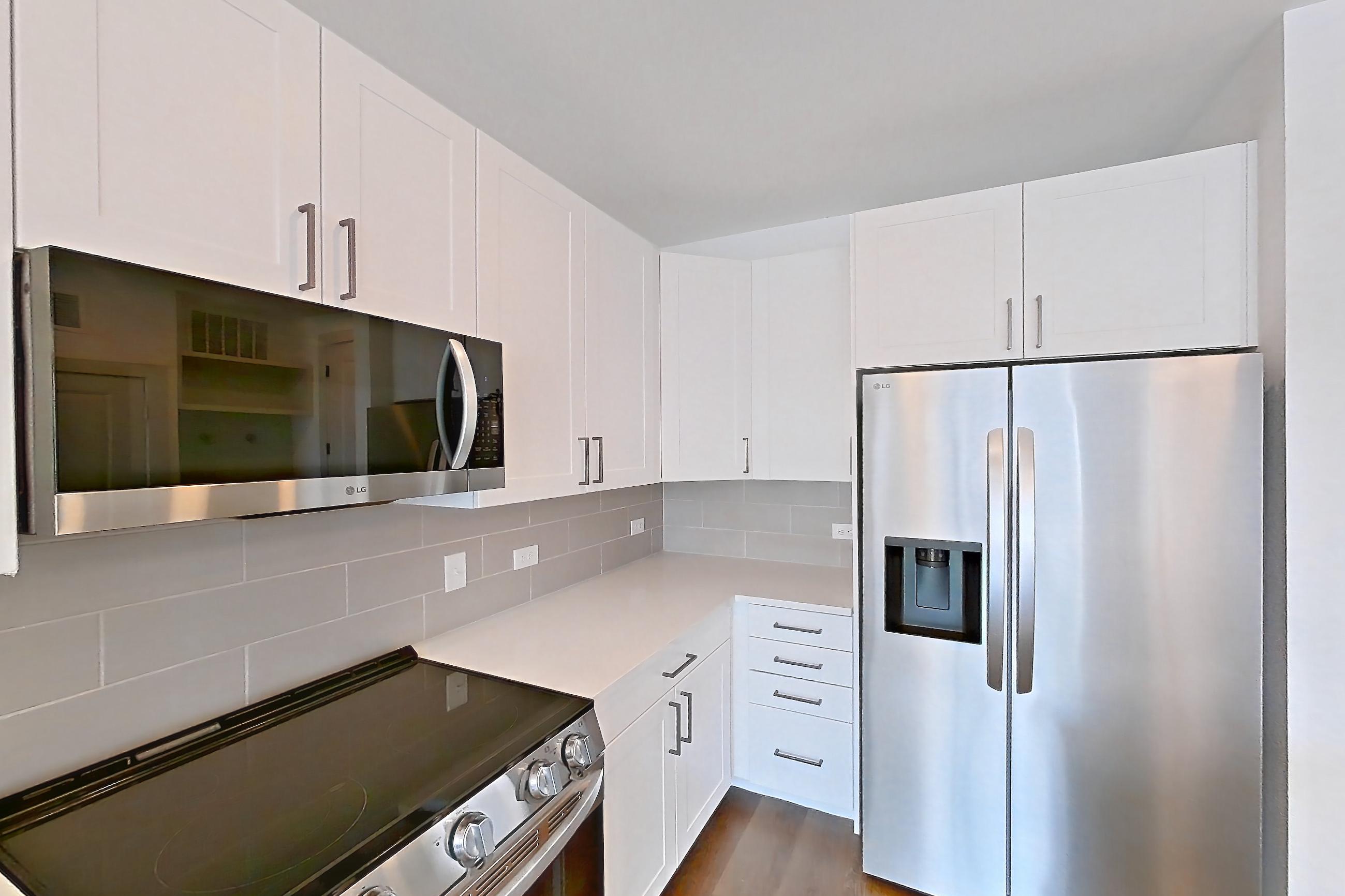 Kitchen with dark wood-finish flooring, electric range, light countertops, light stone countertops, microwave, oven/range, refrigerator, stainless steel appliances, water & ice dispenser, and white appliances, Apartment 2348 at Groves South Congress