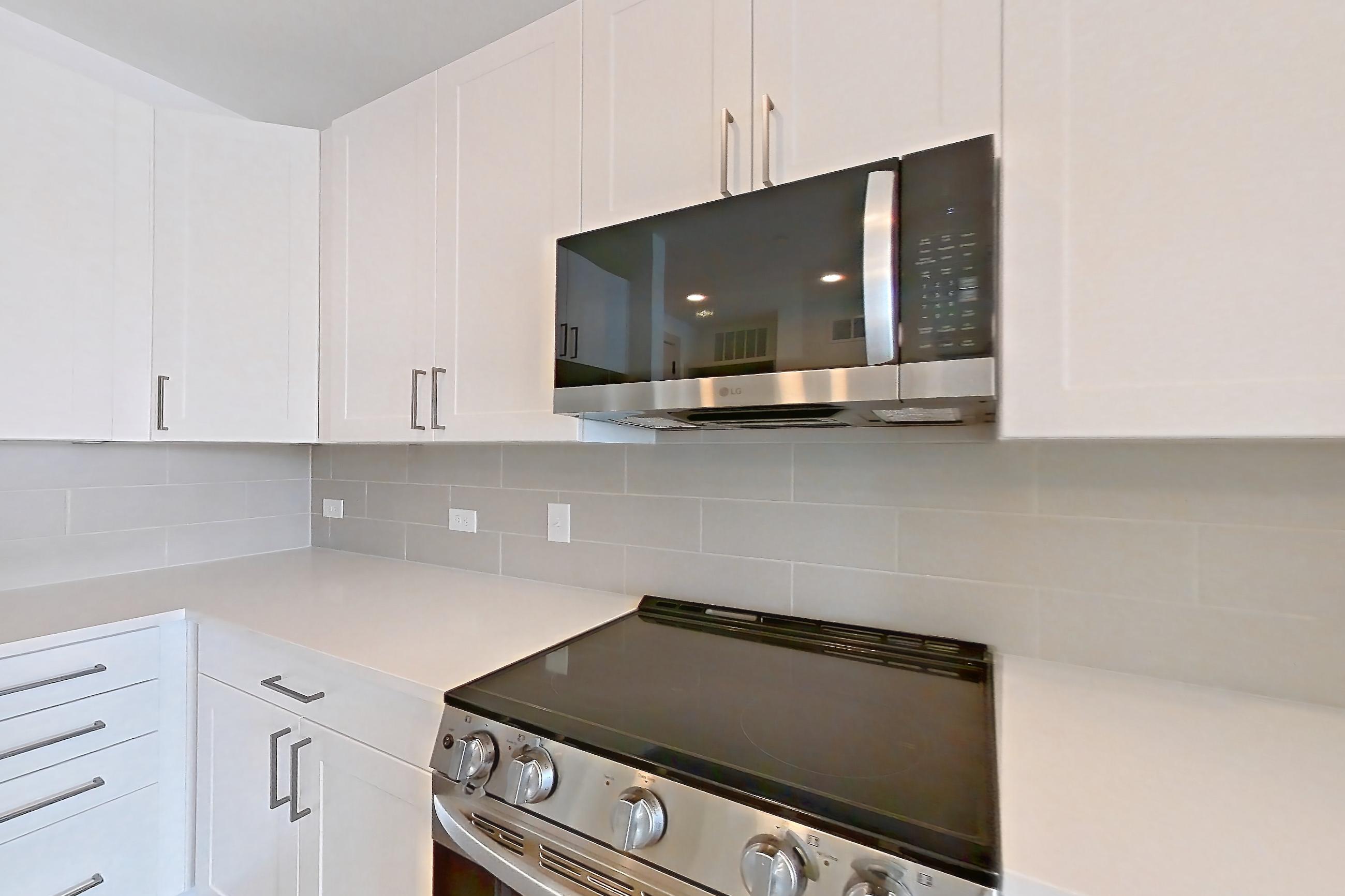 Kitchen with dark wood-finish flooring, dishwasher, electric range, kitchen island, light countertops, light stone countertops, microwave, oven/range, and stainless steel appliances, Apartment 2349 at Groves South Congress