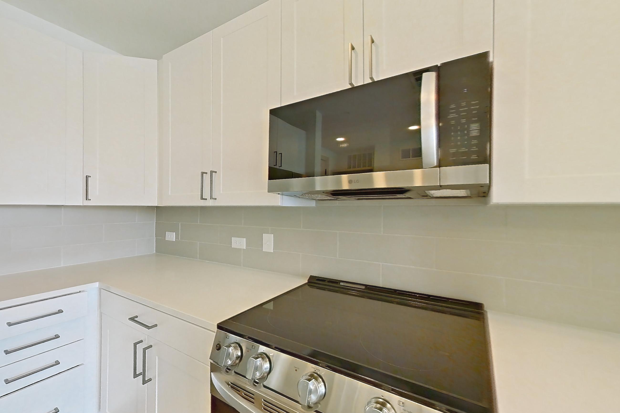 Kitchen with dark wood-finish flooring, dishwasher, electric range, kitchen island, light countertops, light stone countertops, light wood-finish flooring, microwave, oven/range, and stainless steel appliances, Apartment 2353 at Groves South Congress