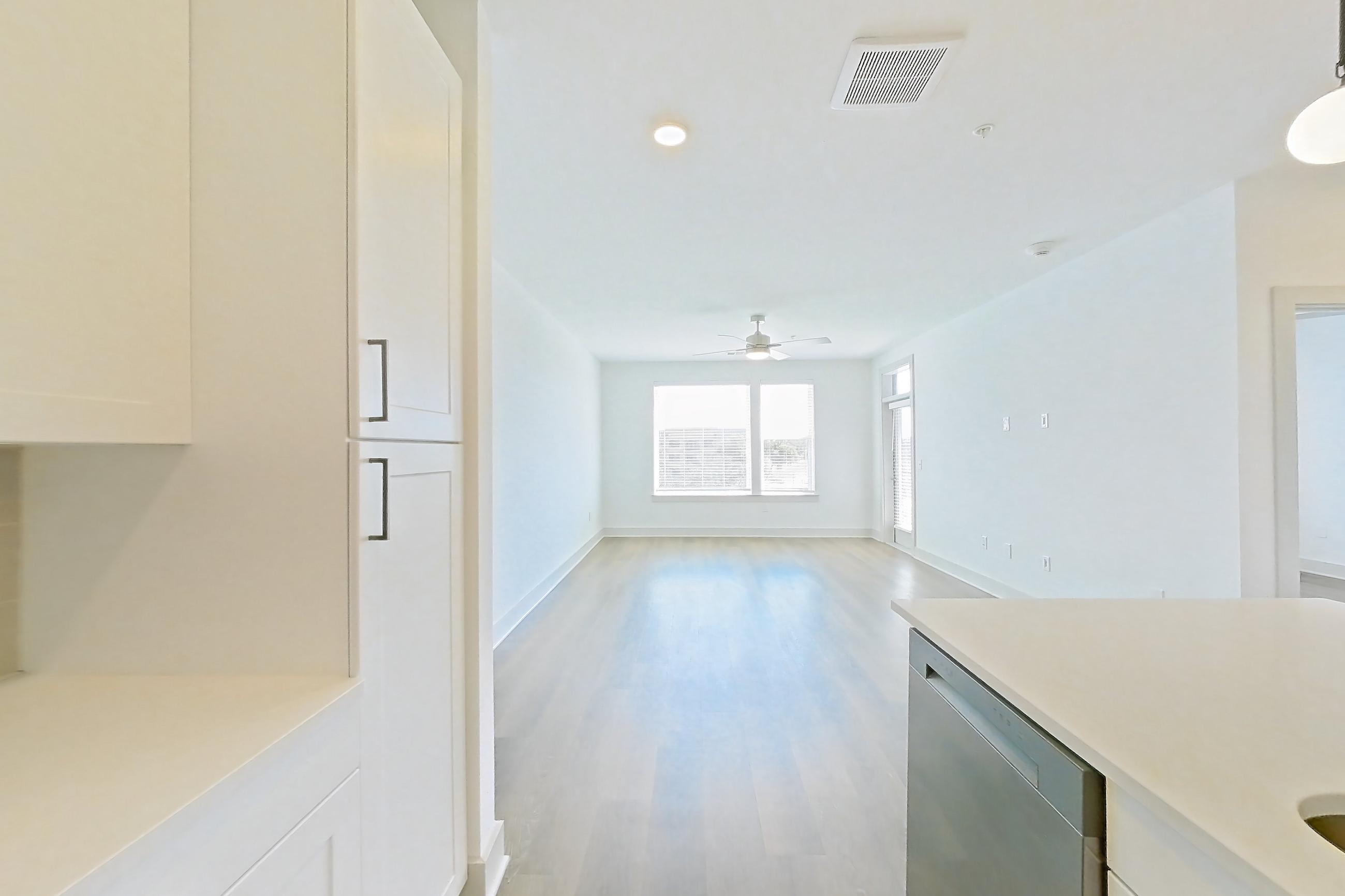 Kitchen with dark wood-finish flooring, dishwasher, electric range, kitchen island, light countertops, light stone countertops, light wood-finish flooring, microwave, oven/range, and stainless steel appliances, Apartment 2353 at Groves South Congress