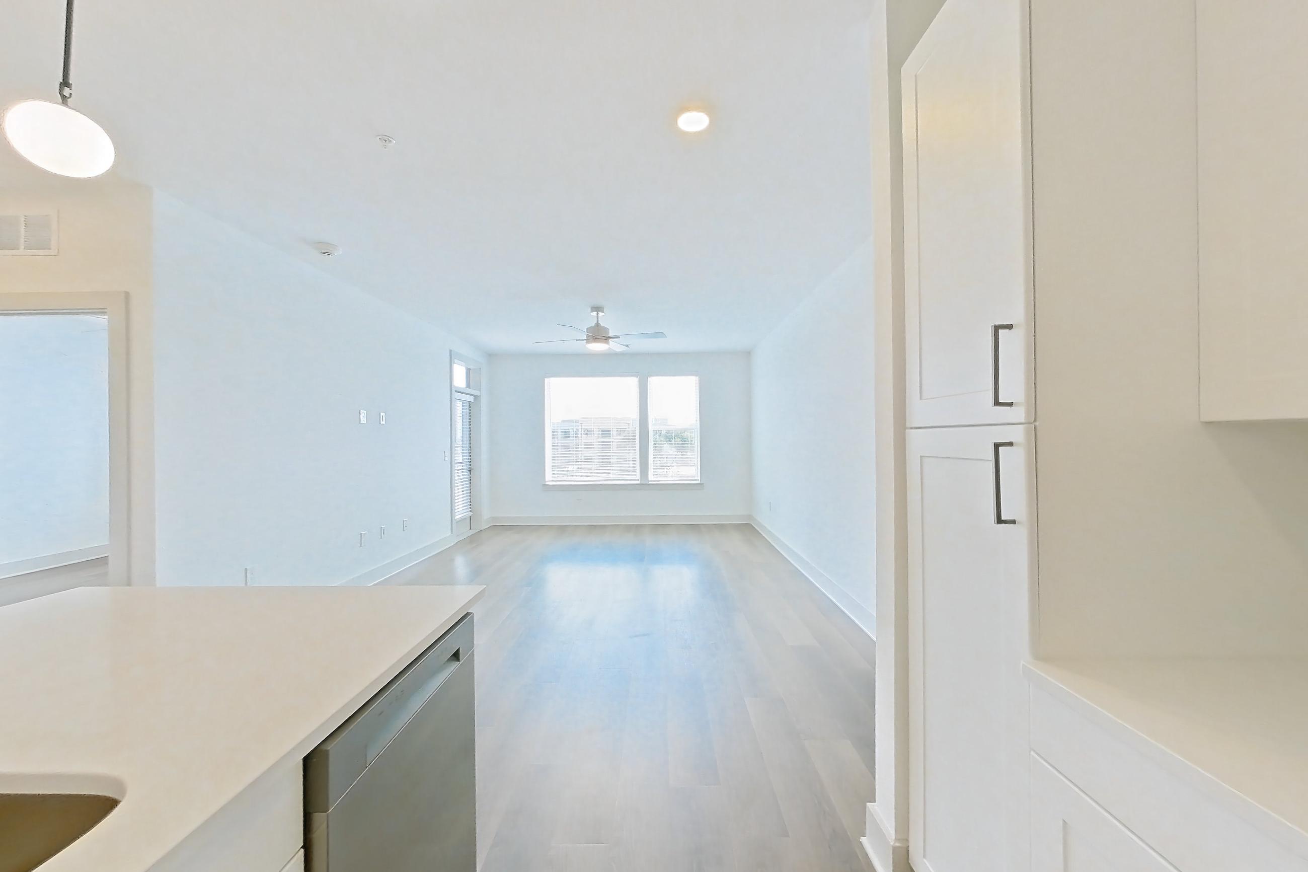 Kitchen with dark wood-finish flooring, dishwasher, electric range, kitchen island, light countertops, light stone countertops, light wood-finish flooring, oven/range, and stainless steel appliances, Apartment 2355 at Groves South Congress