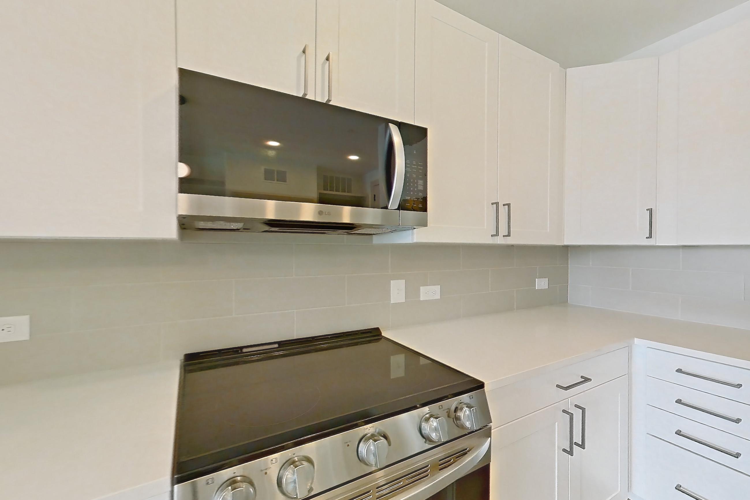 Kitchen with dark wood-finish flooring, dishwasher, electric range, kitchen island, light countertops, light stone countertops, light wood-finish flooring, oven/range, and stainless steel appliances, Apartment 2355 at Groves South Congress