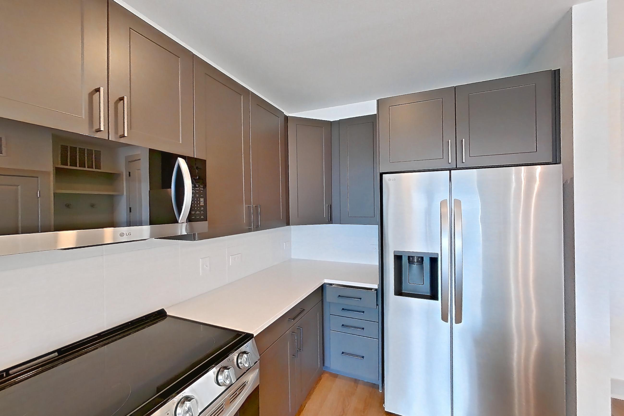 Kitchen with dark wood-finish flooring, electric range, light countertops, light stone countertops, light wood-finish flooring, oven/range, refrigerator, stainless steel appliances, and water & ice dispenser, Apartment 2455 at Groves South Congress