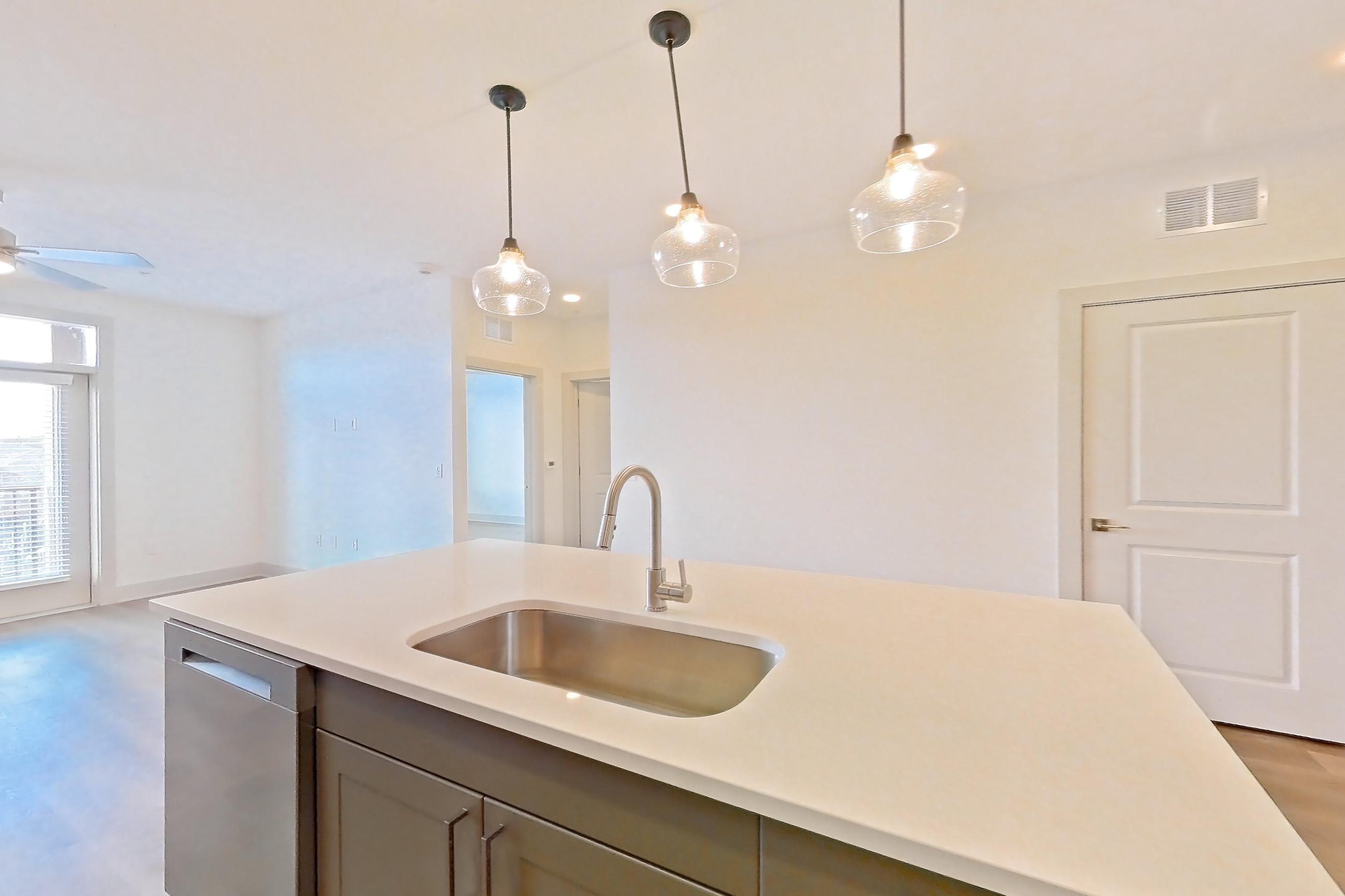 Kitchen with dishwasher, electric range, light countertops, light stone countertops, light wood-finish flooring, microwave, oven/range, and stainless steel appliances, Apartment 2208 at Groves South Congress