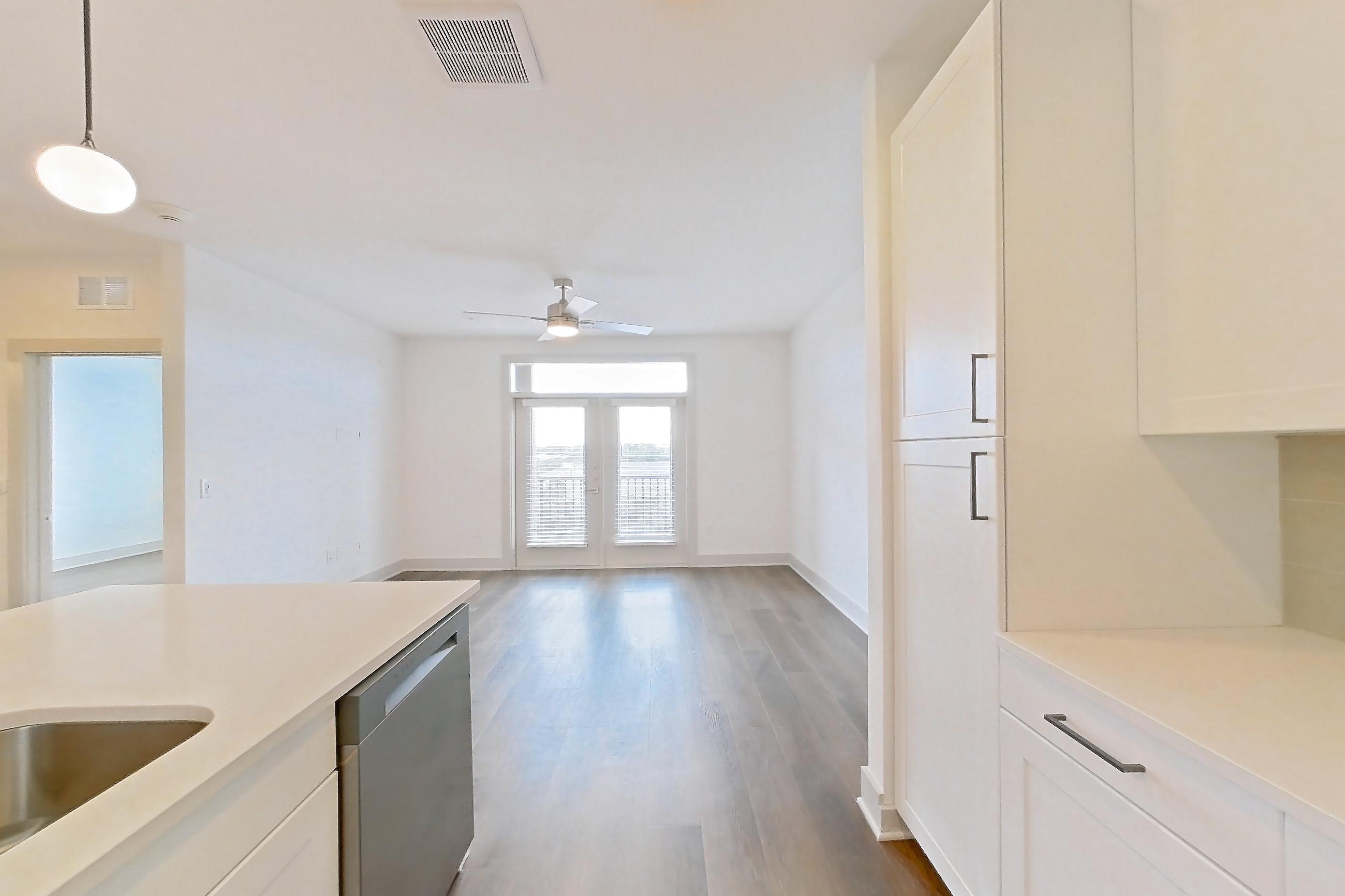 Kitchen with dark wood-finish flooring, dishwasher, electric range, kitchen island, light countertops, light stone countertops, oven/range, and stainless steel appliances, Apartment 2306 at Groves South Congress