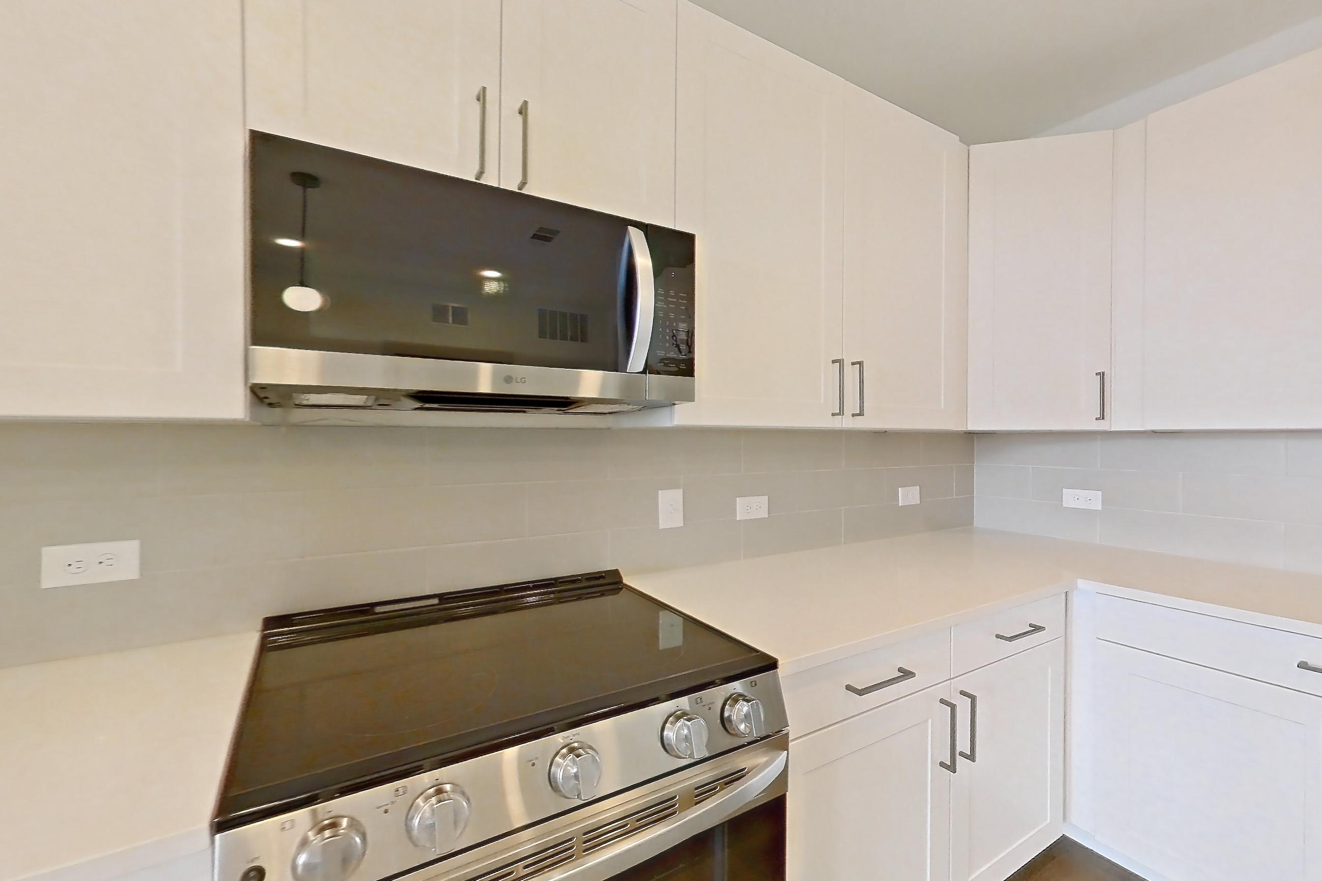 Kitchen with dark wood-finish flooring, dishwasher, electric range, kitchen island, light countertops, light stone countertops, oven/range, and stainless steel appliances, Apartment 2306 at Groves South Congress