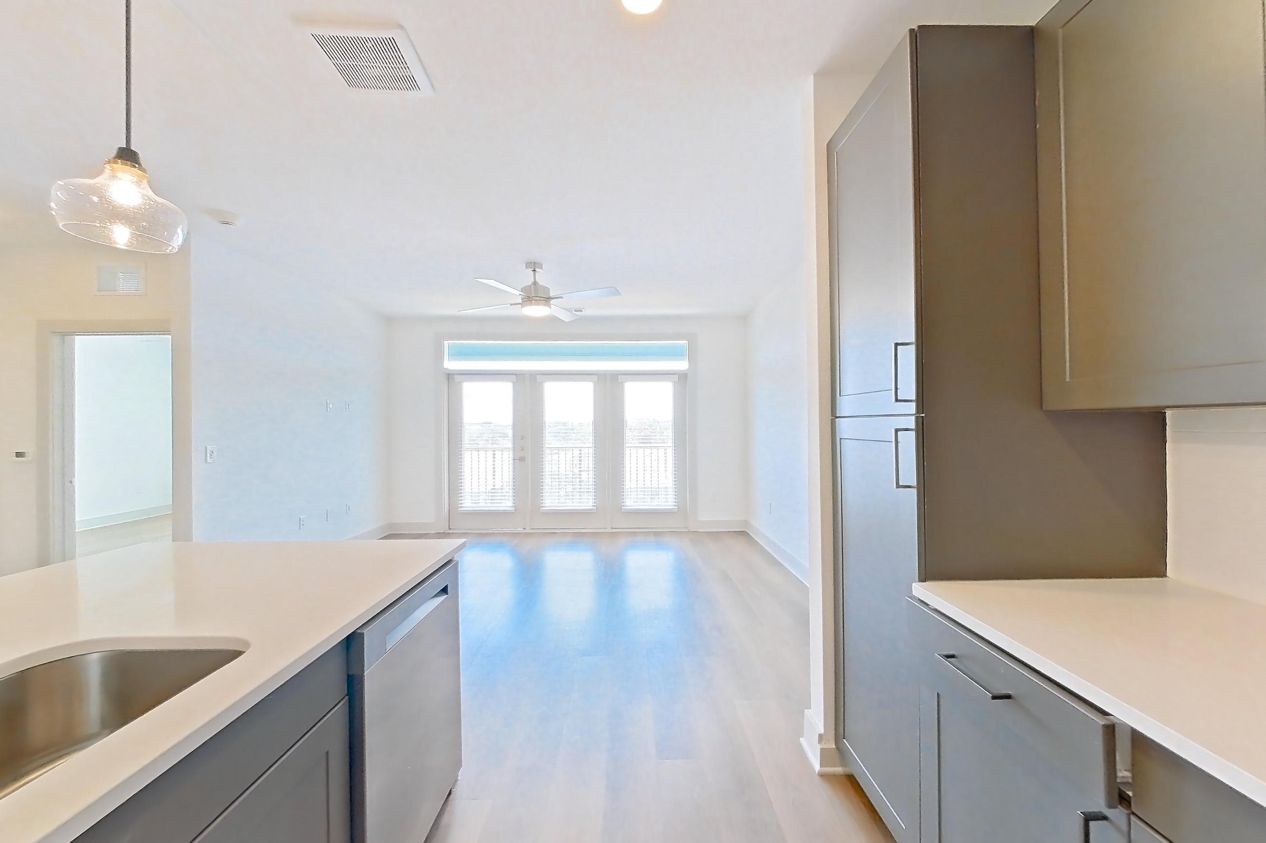 Kitchen with dishwasher, electric range, kitchen island, light countertops, light stone countertops, light wood-finish flooring, oven/range, and stainless steel appliances, Apartment 2404 at Groves South Congress