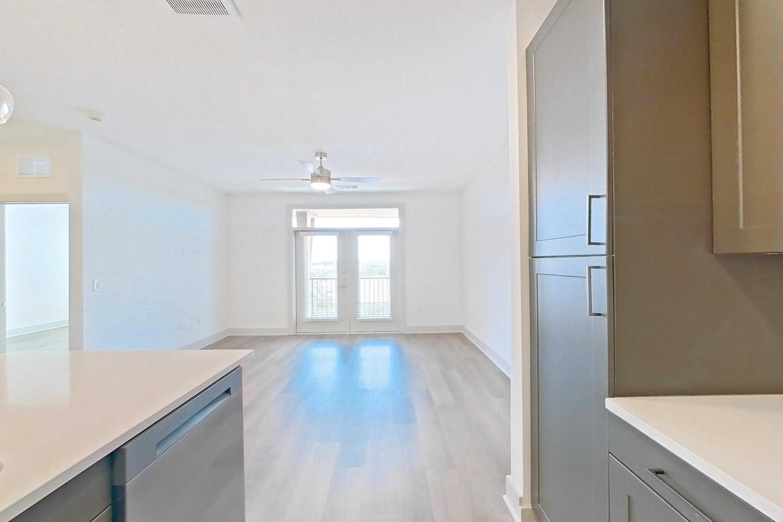 Kitchen with dishwasher, electric range, kitchen island, light countertops, light stone countertops, light wood-finish flooring, oven/range, and stainless steel appliances, Apartment 2406 at Groves South Congress