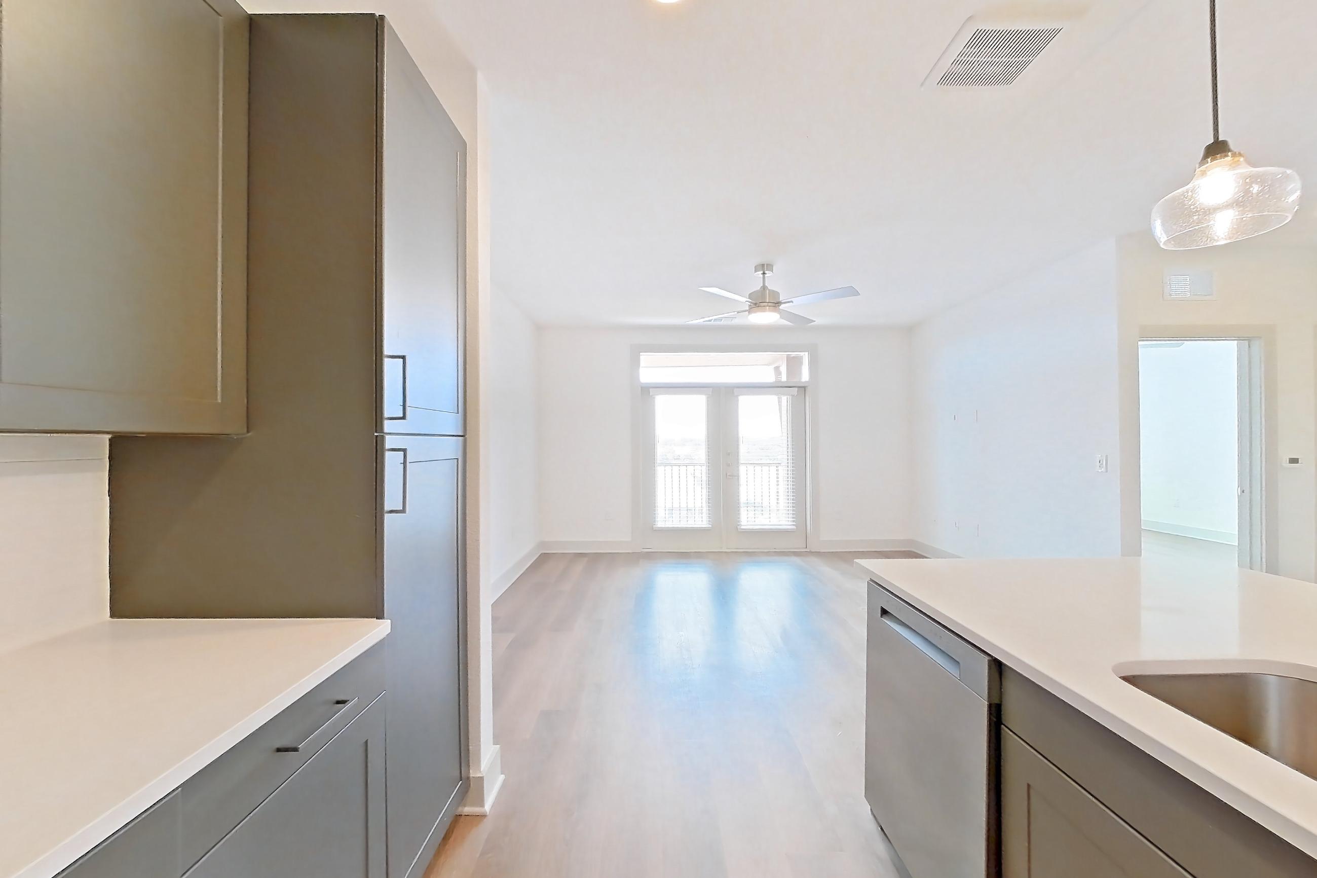 Kitchen with dishwasher, electric range, light countertops, light stone countertops, light wood-finish flooring, microwave, oven/range, and stainless steel appliances, Apartment 2408 at Groves South Congress