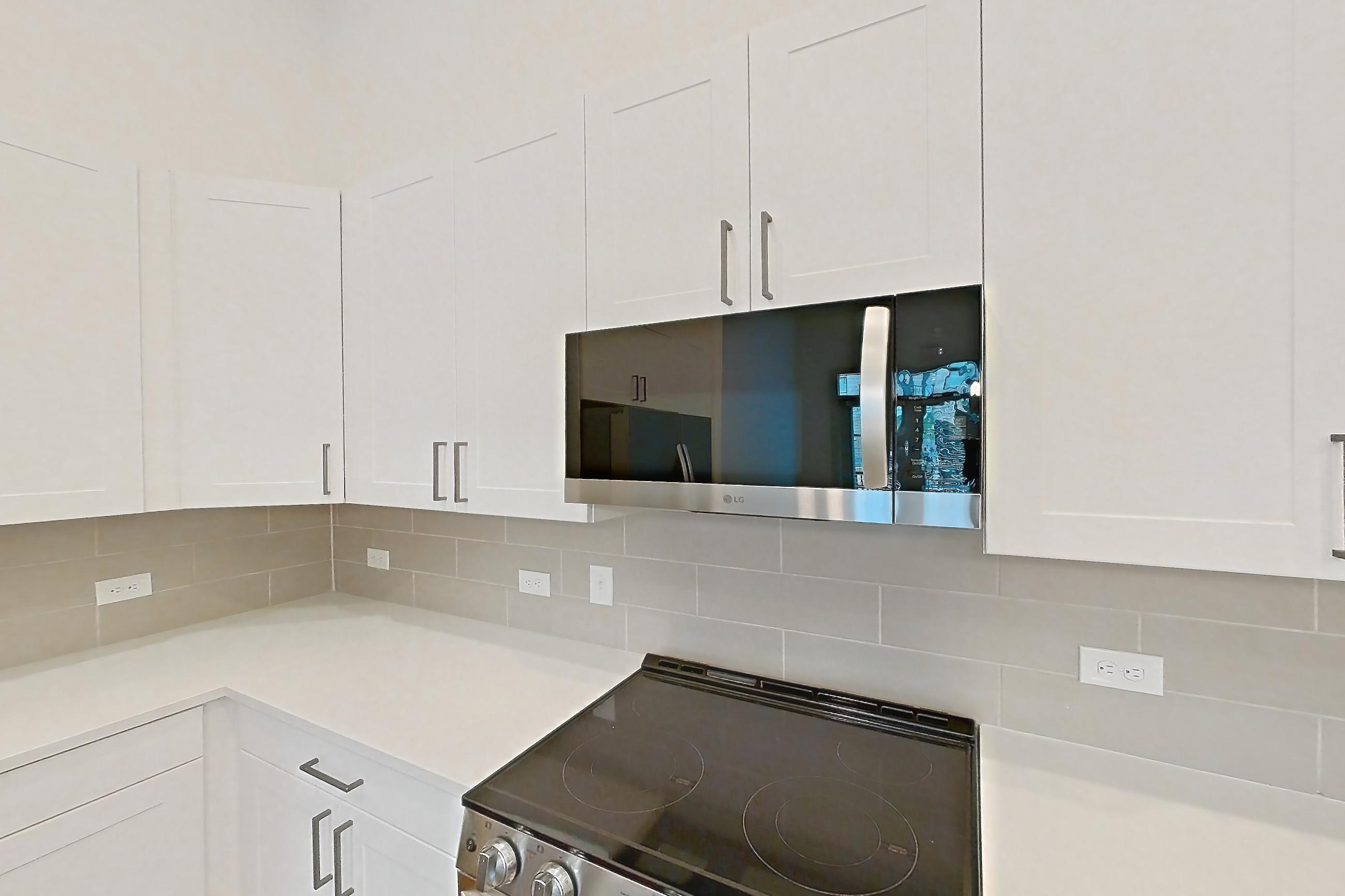 Kitchen with dark wood-finish flooring, electric range, light countertops, light stone countertops, microwave, oven/range, refrigerator, stainless steel appliances, and water & ice dispenser, Apartment 2145 at Groves South Congress