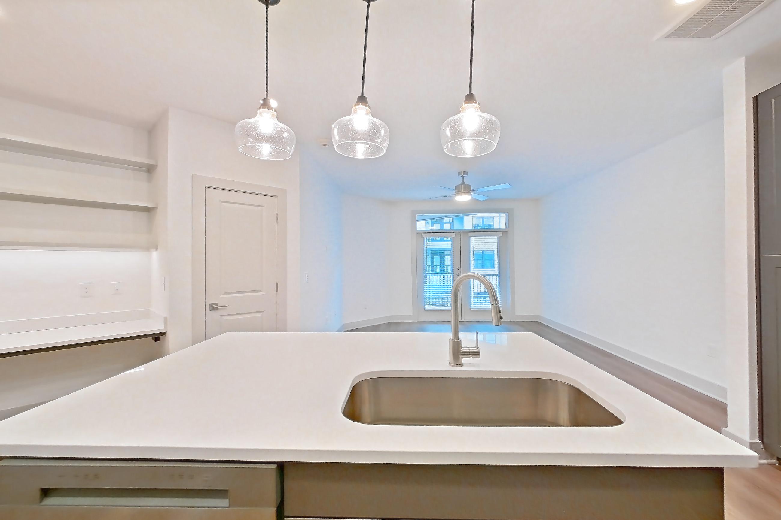 Kitchen with dishwasher, kitchen island, light countertops, light stone countertops, light wood-finish flooring, microwave, oven/range, refrigerator, stainless steel appliances, and water & ice dispenser, Apartment 2245 at Groves South Congress