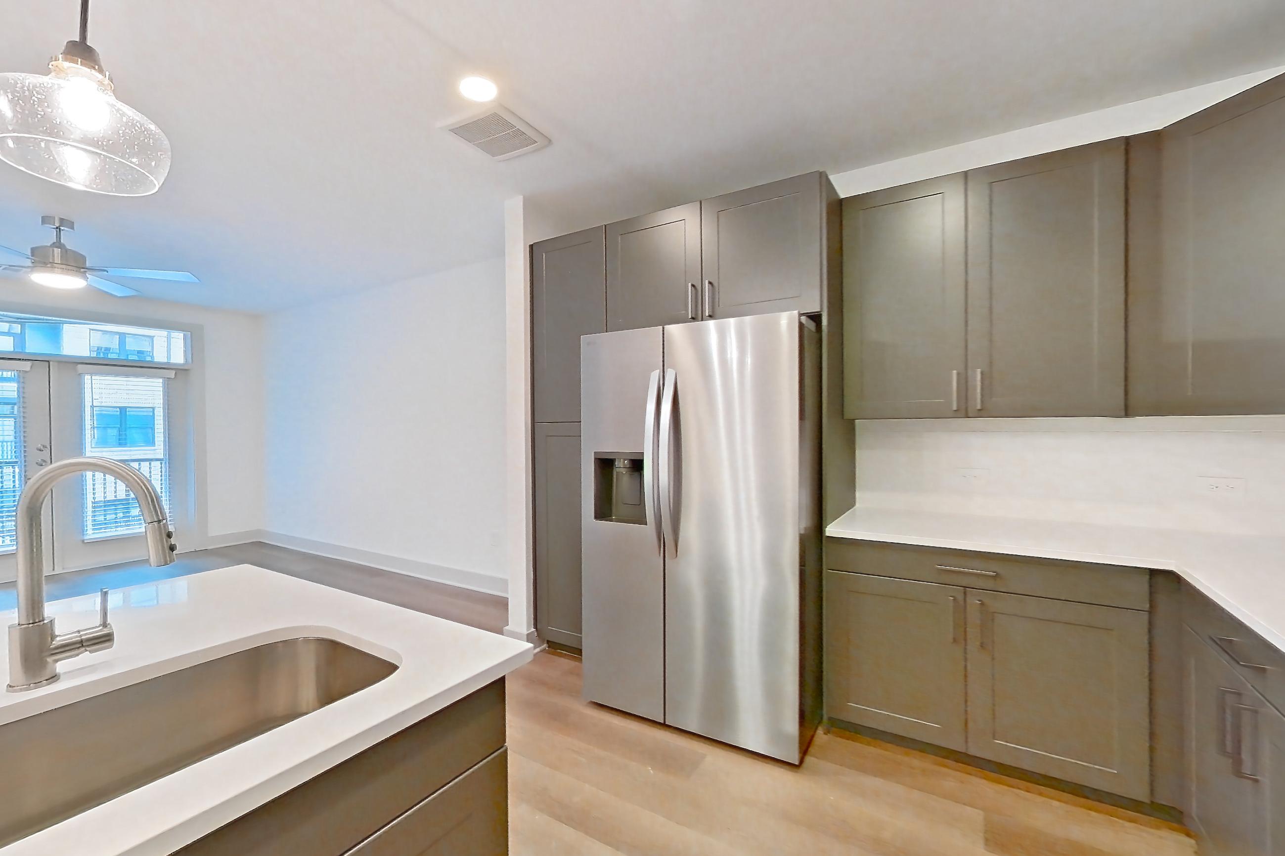 Kitchen with dishwasher, kitchen island, light countertops, light stone countertops, light wood-finish flooring, microwave, oven/range, refrigerator, stainless steel appliances, and water & ice dispenser, Apartment 2245 at Groves South Congress