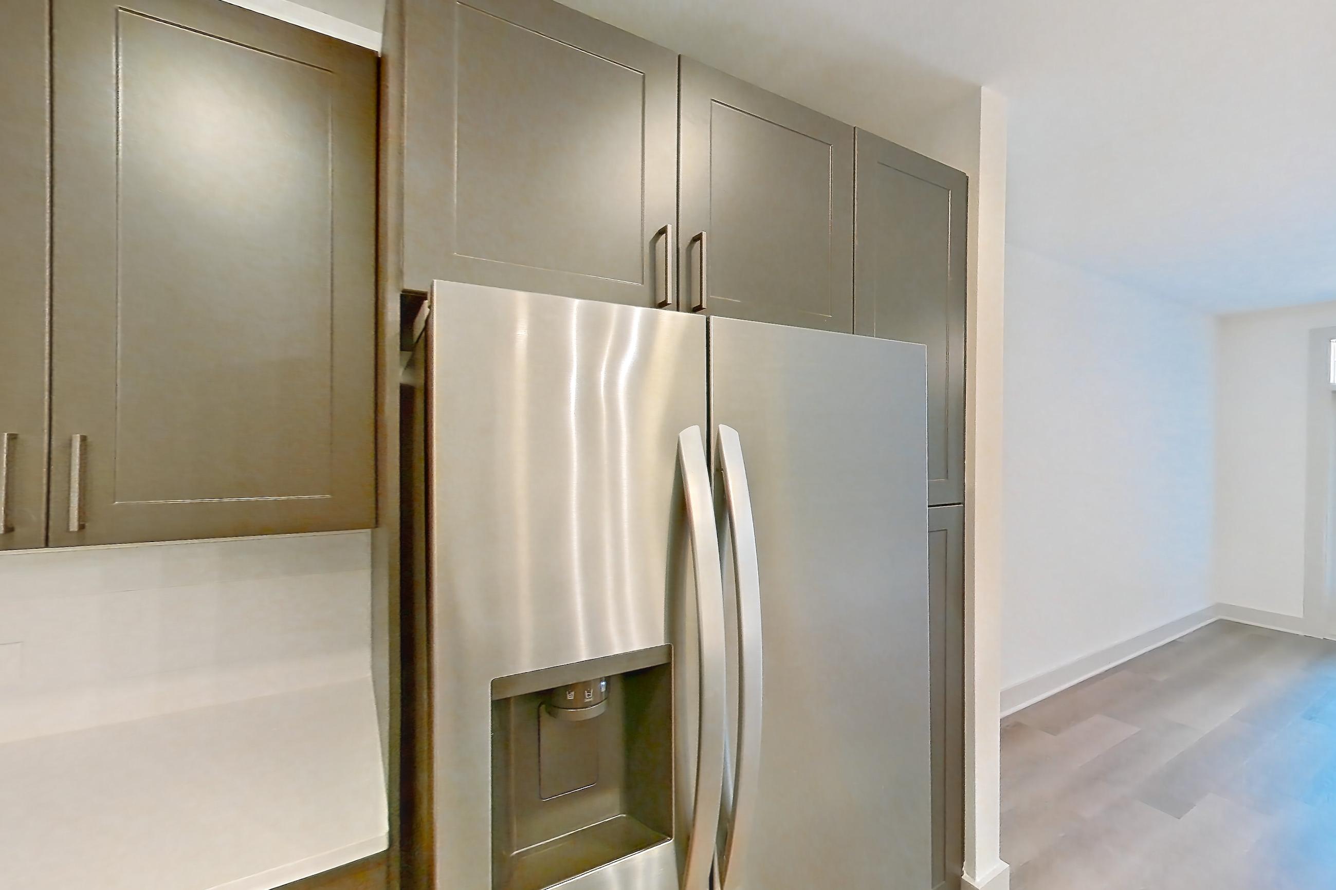 Kitchen with electric range, kitchen island, light countertops, light stone countertops, light wood-finish flooring, oven/range, range hood, refrigerator, stainless steel appliances, and water & ice dispenser, Apartment 2250 at Groves South Congress