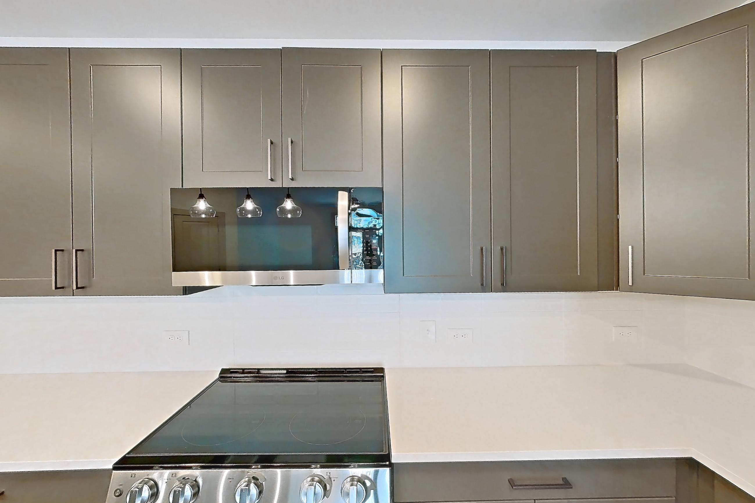 Kitchen with electric range, kitchen island, light countertops, light stone countertops, light wood-finish flooring, oven/range, range hood, refrigerator, stainless steel appliances, and water & ice dispenser, Apartment 2250 at Groves South Congress