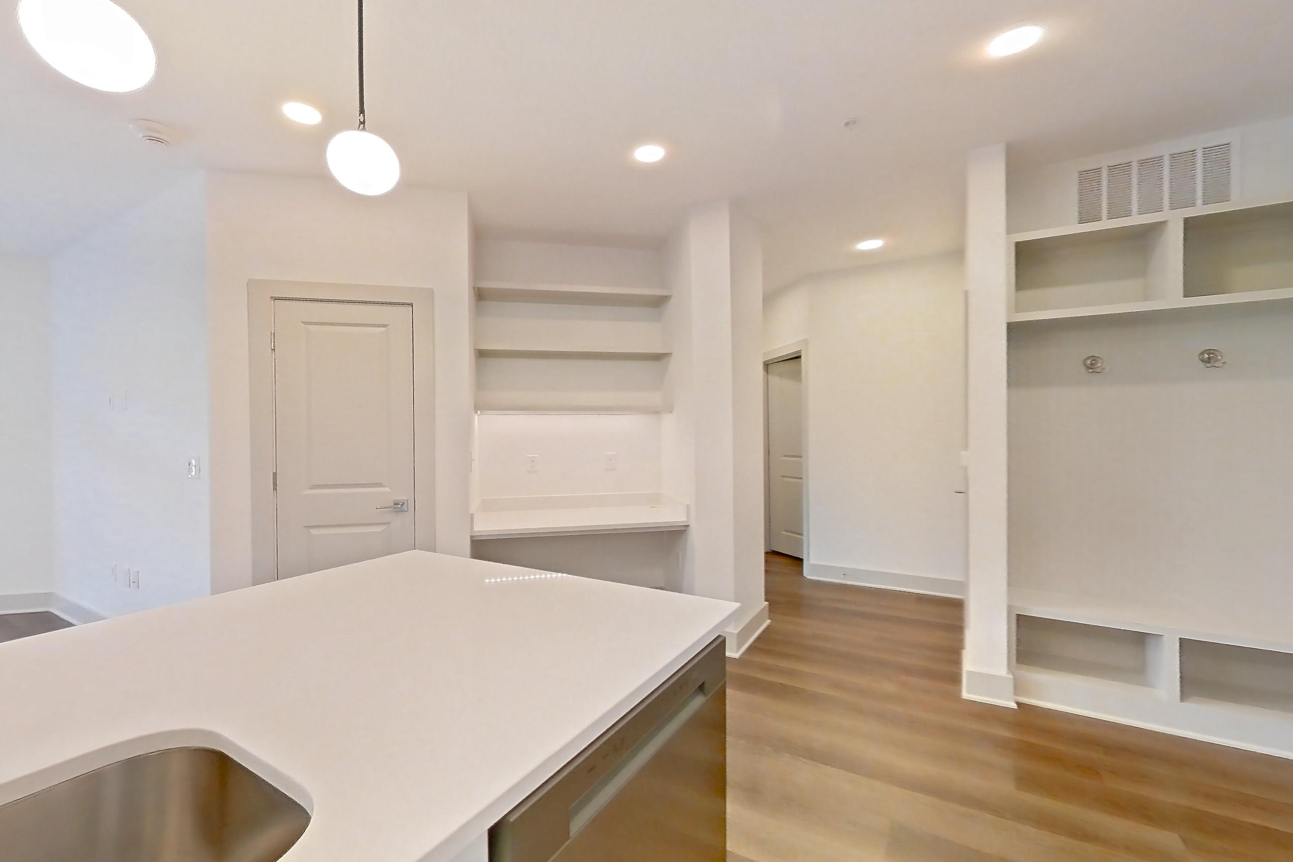 Kitchen with dark wood-finish flooring, dishwasher, electric range, kitchen island, light countertops, light stone countertops, light wood-finish flooring, oven/range, refrigerator, stainless steel appliances, and water & ice dispenser, Apartment 2350 at Groves South Congress