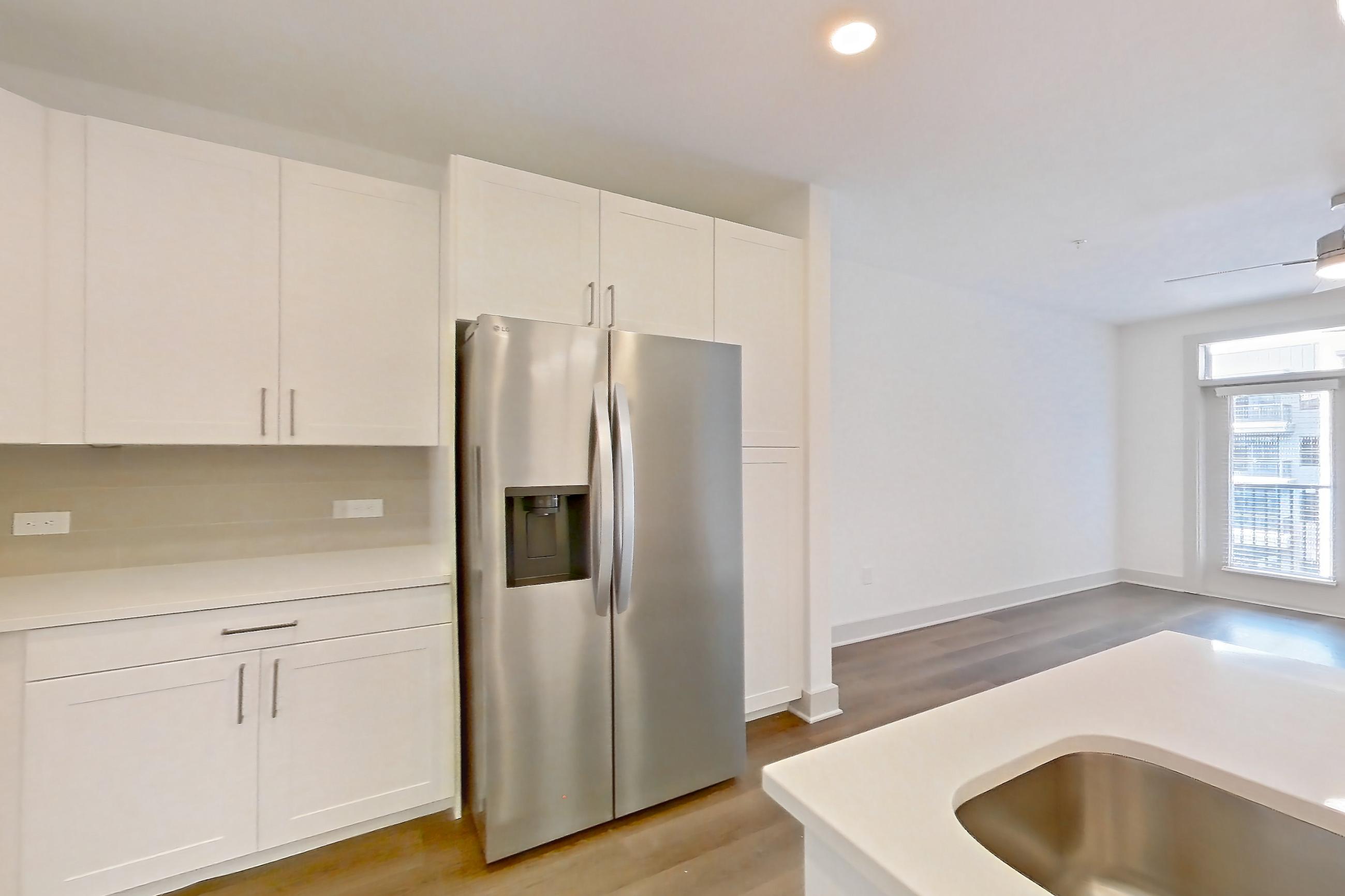 Kitchen with dark wood-finish flooring, dishwasher, electric range, kitchen island, light countertops, light stone countertops, light wood-finish flooring, oven/range, refrigerator, stainless steel appliances, and water & ice dispenser, Apartment 2350 at Groves South Congress