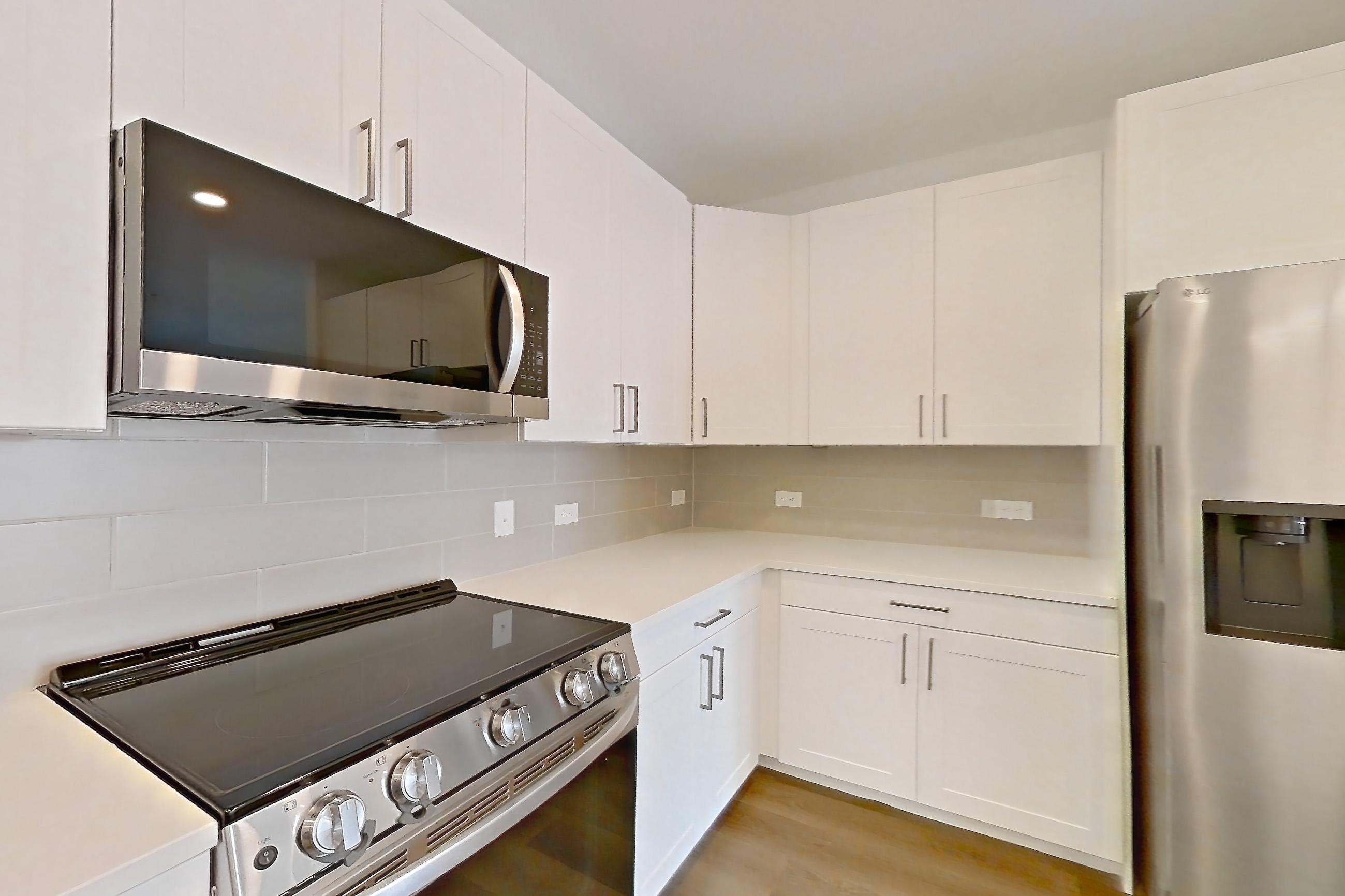 Kitchen with dark wood-finish flooring, dishwasher, electric range, kitchen island, light countertops, light stone countertops, light wood-finish flooring, oven/range, refrigerator, stainless steel appliances, and water & ice dispenser, Apartment 2350 at Groves South Congress