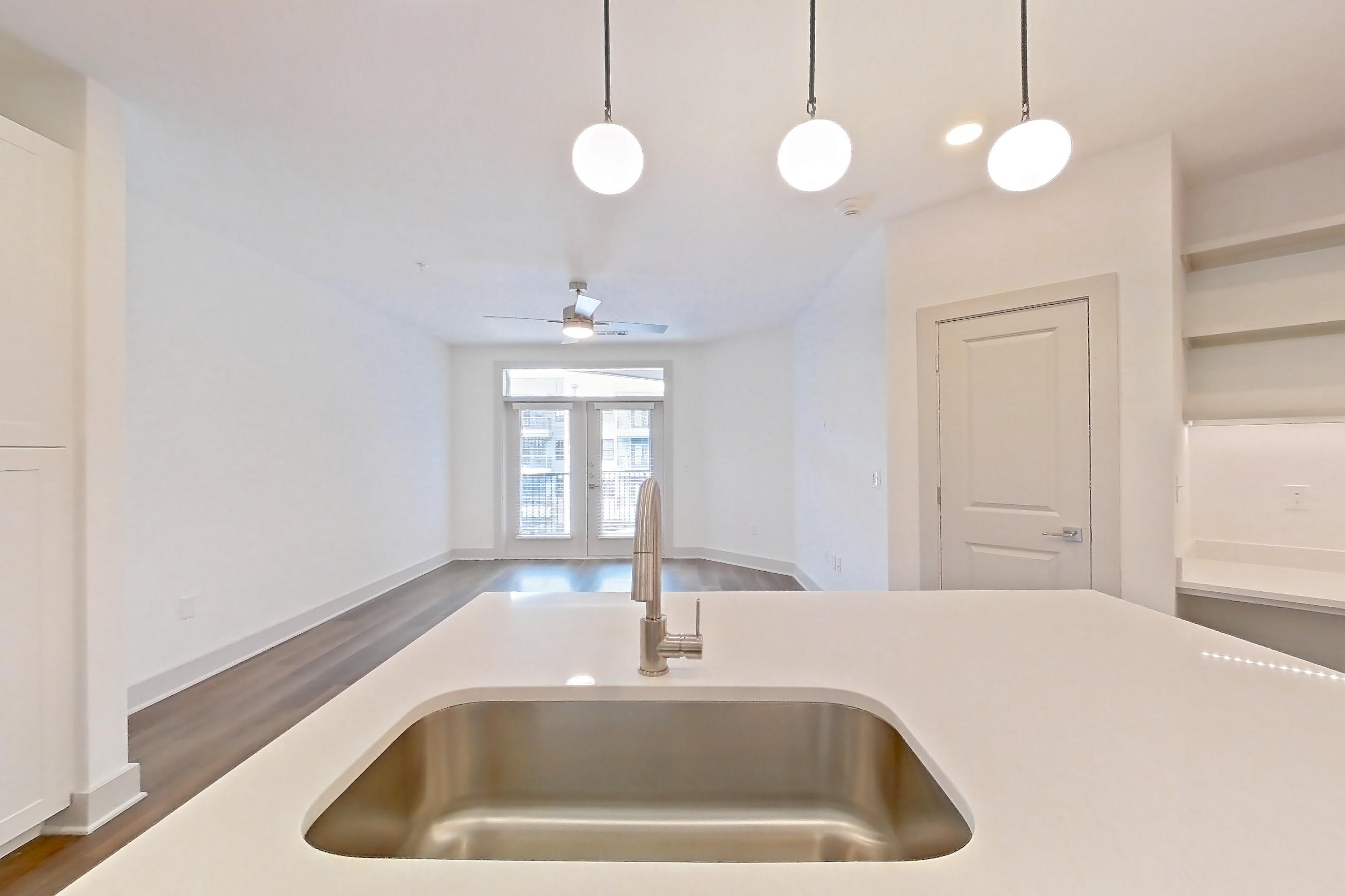 Kitchen with dark wood-finish flooring, dishwasher, electric range, kitchen island, light countertops, light stone countertops, light wood-finish flooring, oven/range, refrigerator, stainless steel appliances, and water & ice dispenser, Apartment 2350 at Groves South Congress