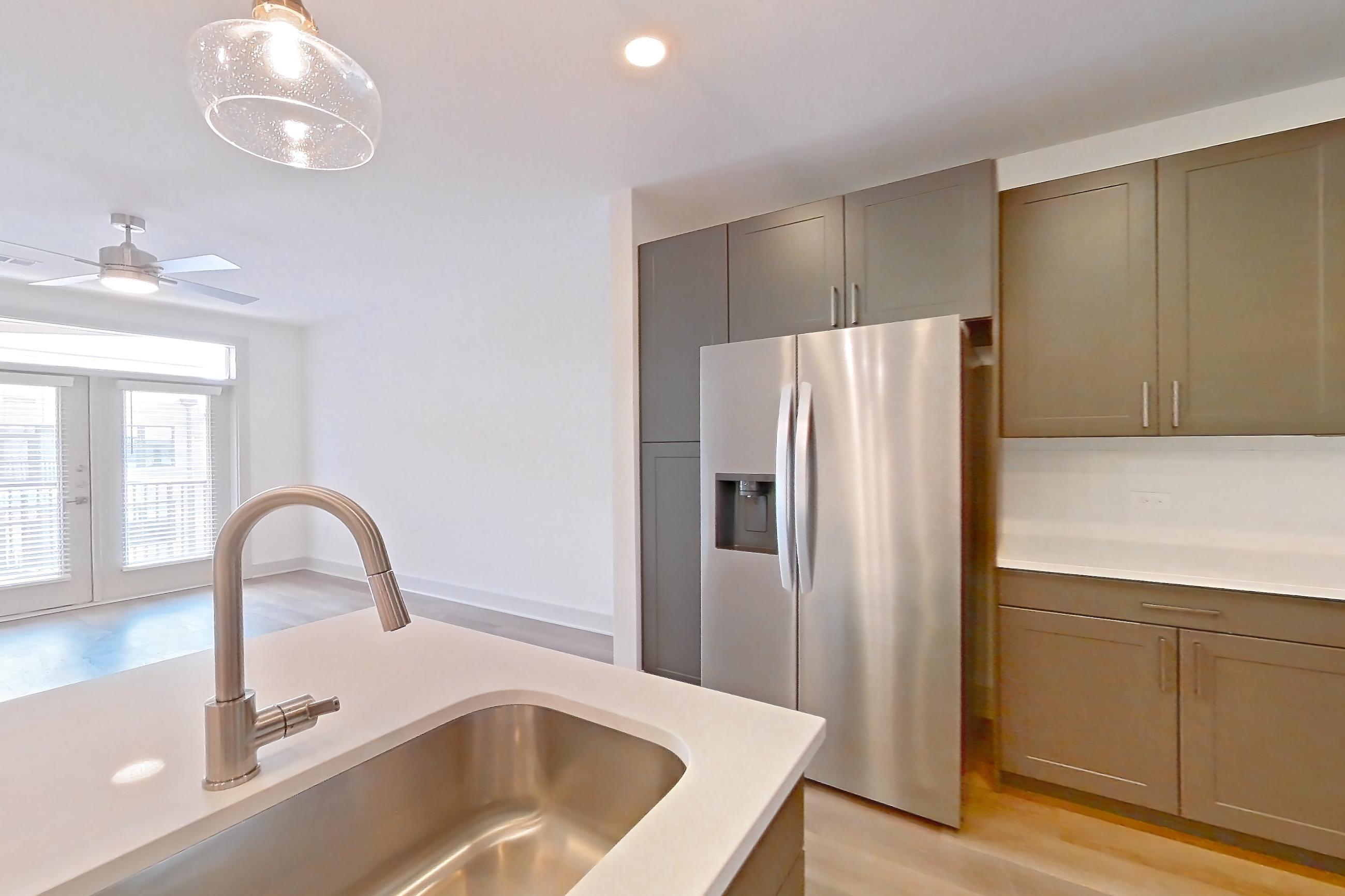 Kitchen with electric range, kitchen island, light countertops, light stone countertops, light wood-finish flooring, oven/range, refrigerator, stainless steel appliances, water & ice dispenser, and white appliances, Apartment 2445 at Groves South Congress