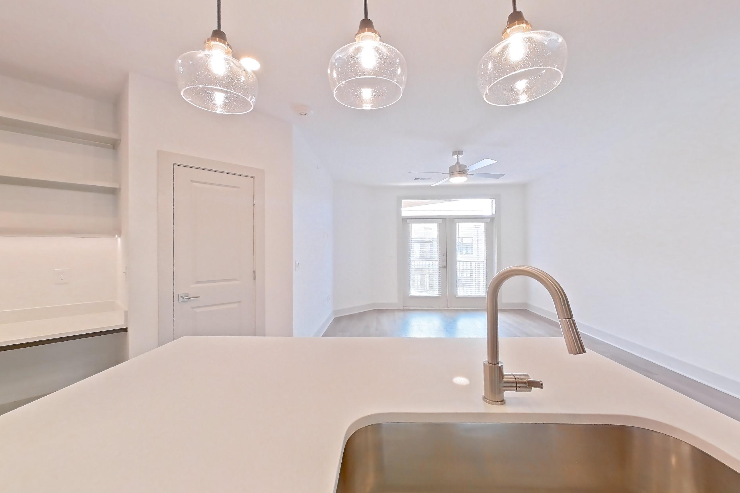 Kitchen with electric range, kitchen island, light countertops, light stone countertops, light wood-finish flooring, oven/range, refrigerator, stainless steel appliances, water & ice dispenser, and white appliances, Apartment 2445 at Groves South Congress