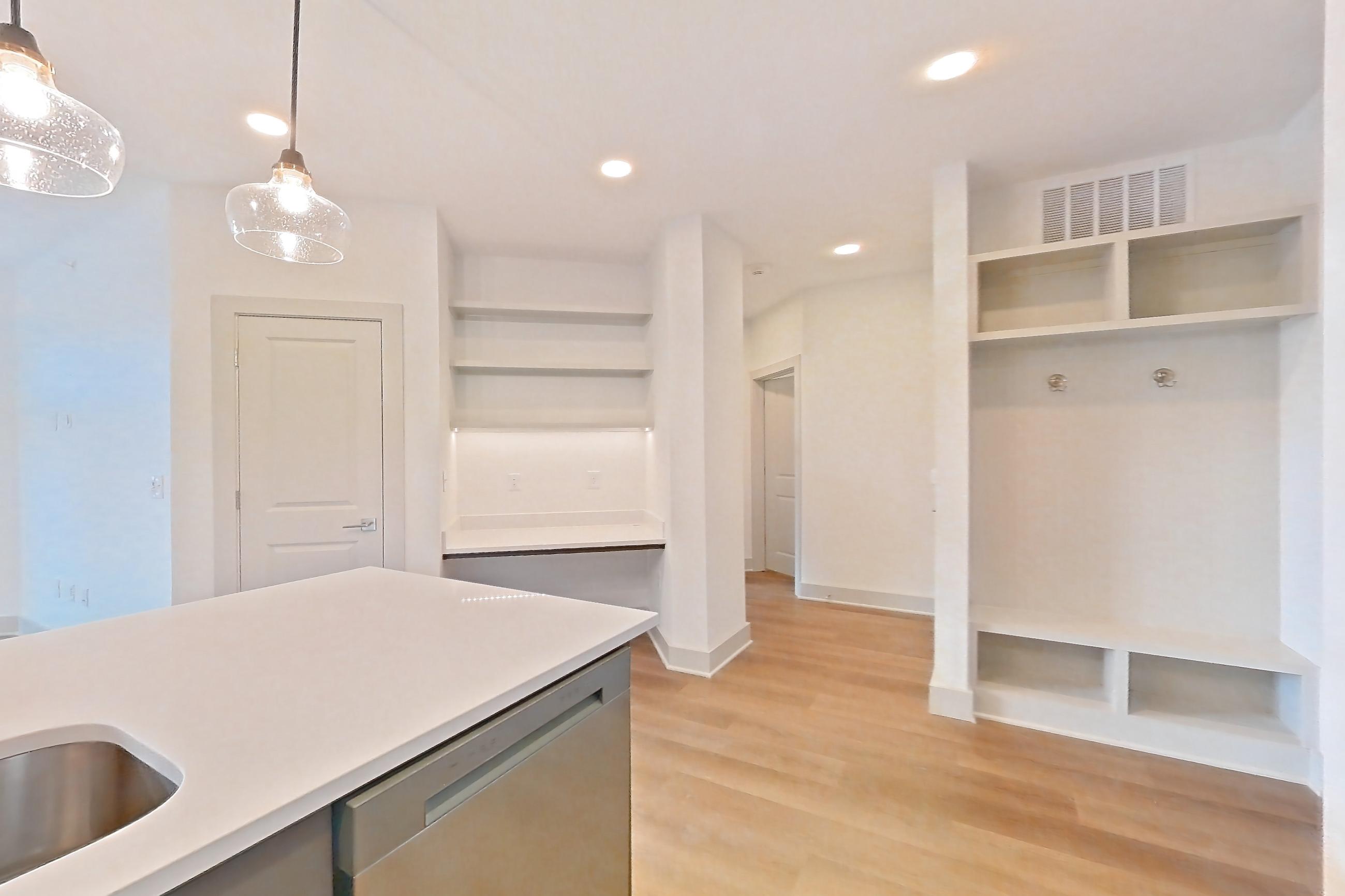 Kitchen with dishwasher, electric range, kitchen island, light countertops, light stone countertops, light wood-finish flooring, oven/range, refrigerator, stainless steel appliances, and water & ice dispenser, Apartment 2450 at Groves South Congress
