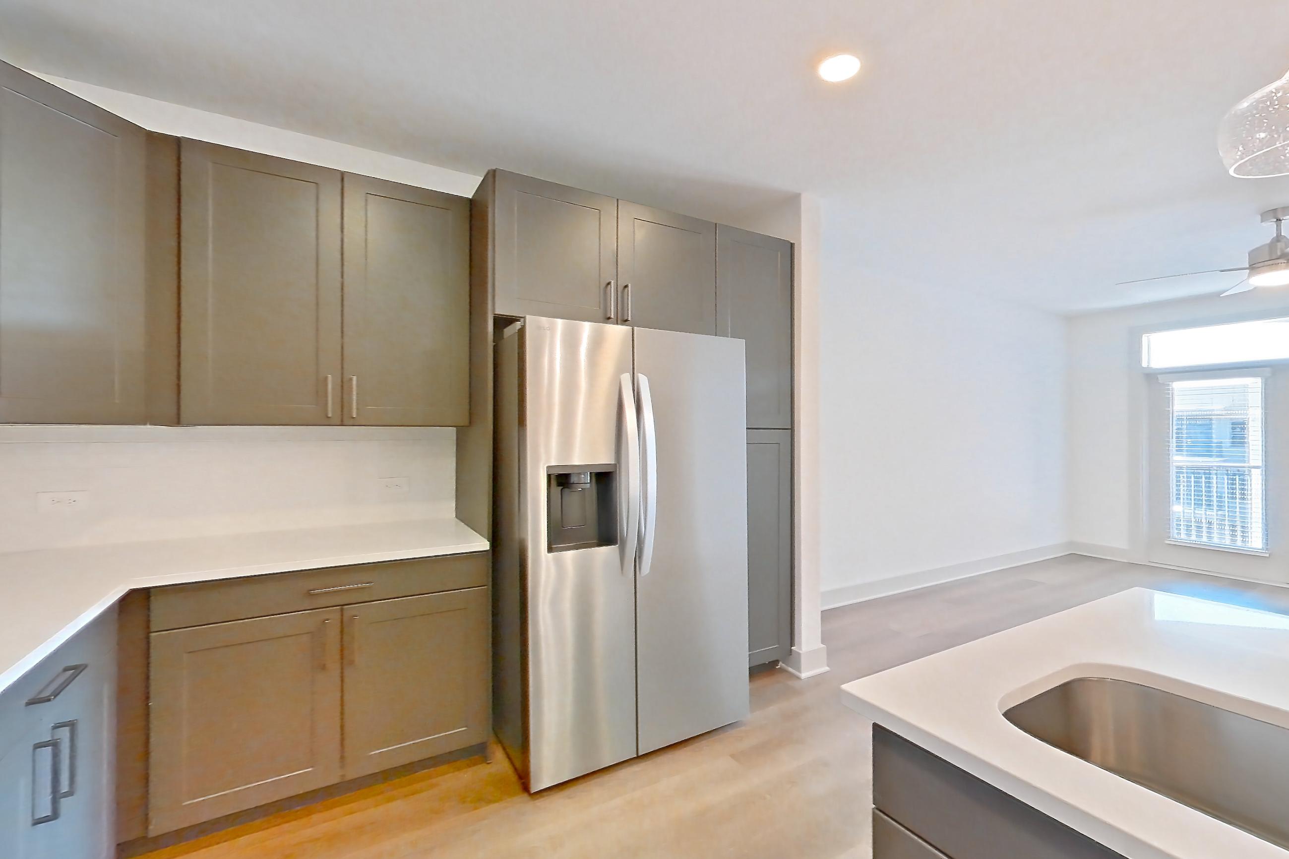 Kitchen with dishwasher, electric range, kitchen island, light countertops, light stone countertops, light wood-finish flooring, oven/range, refrigerator, stainless steel appliances, and water & ice dispenser, Apartment 2450 at Groves South Congress