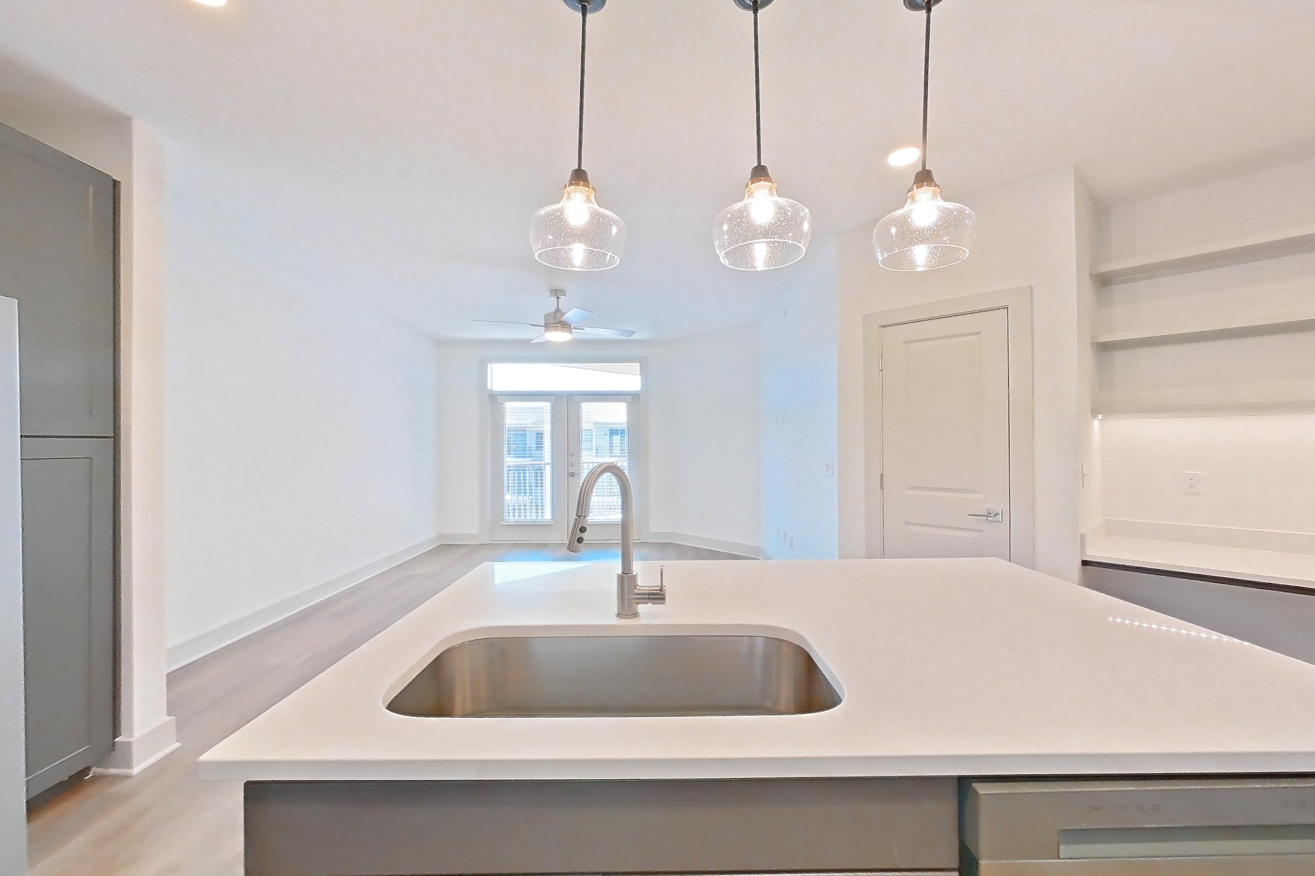 Kitchen with dishwasher, electric range, kitchen island, light countertops, light stone countertops, light wood-finish flooring, oven/range, refrigerator, stainless steel appliances, and water & ice dispenser, Apartment 2450 at Groves South Congress