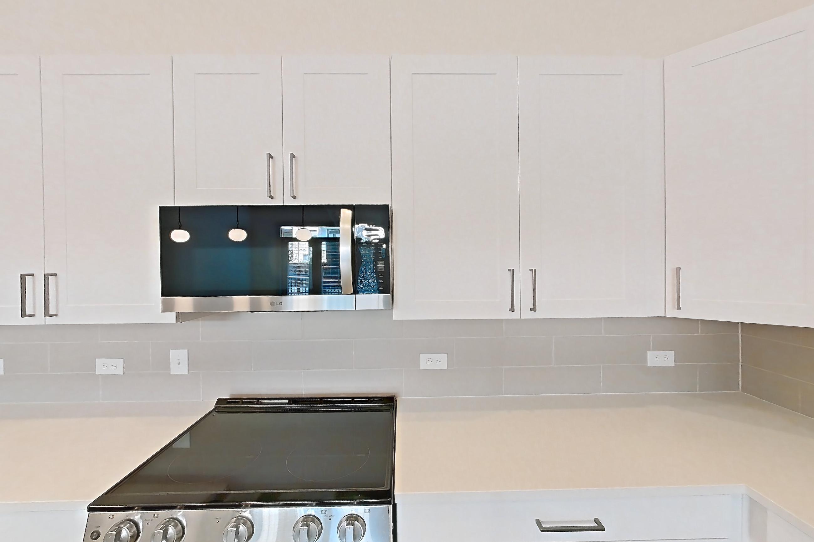 Kitchen with dark wood-finish flooring, electric range, kitchen island, light countertops, light stone countertops, microwave, oven/range, refrigerator, stainless steel appliances, and water & ice dispenser, Apartment 2152 at Groves South Congress