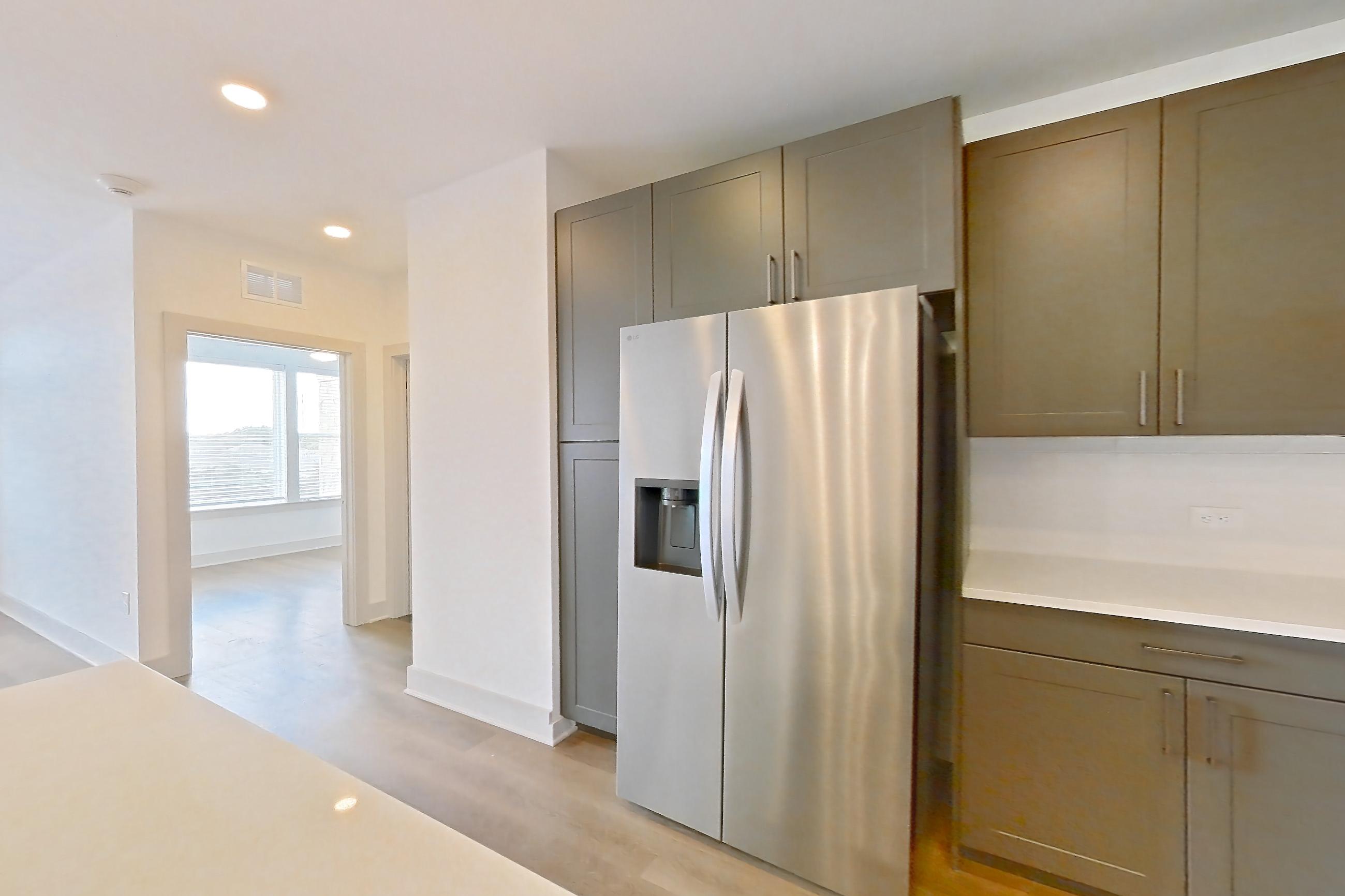 Kitchen with light countertops, light stone countertops, light wood-finish flooring, oven/range, refrigerator, stainless steel appliances, and water & ice dispenser, Apartment 2202 at Groves South Congress