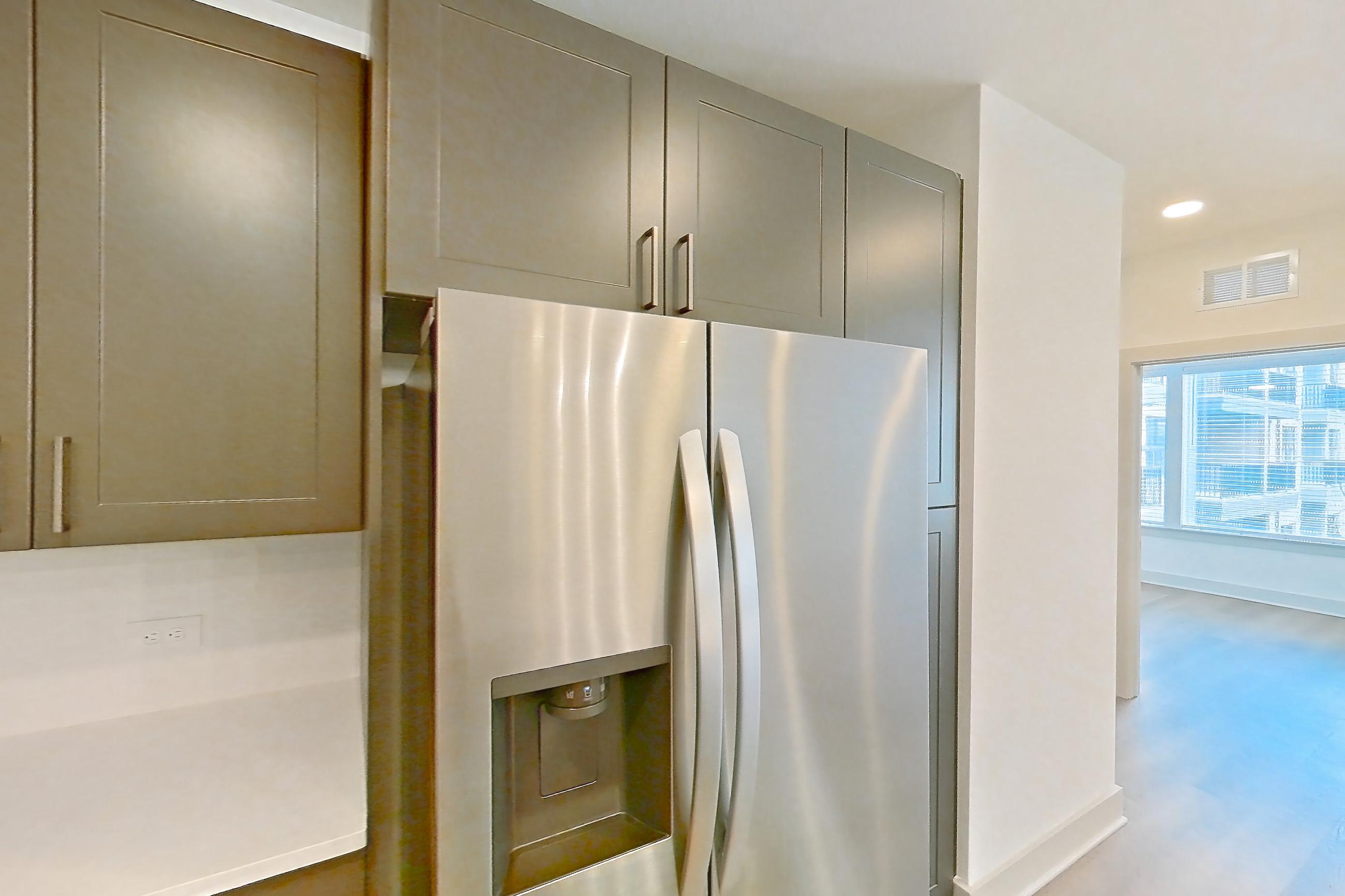 Kitchen with electric range, kitchen island, light countertops, light stone countertops, light wood-finish flooring, oven/range, range hood, refrigerator, stainless steel appliances, and water & ice dispenser, Apartment 2252 at Groves South Congress