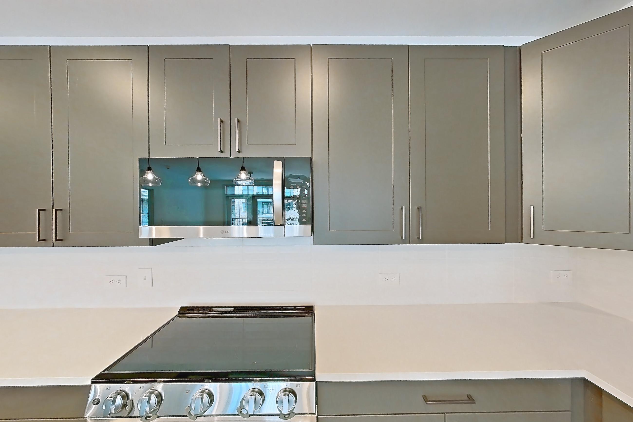 Kitchen with electric range, kitchen island, light countertops, light stone countertops, light wood-finish flooring, oven/range, range hood, refrigerator, stainless steel appliances, and water & ice dispenser, Apartment 2252 at Groves South Congress