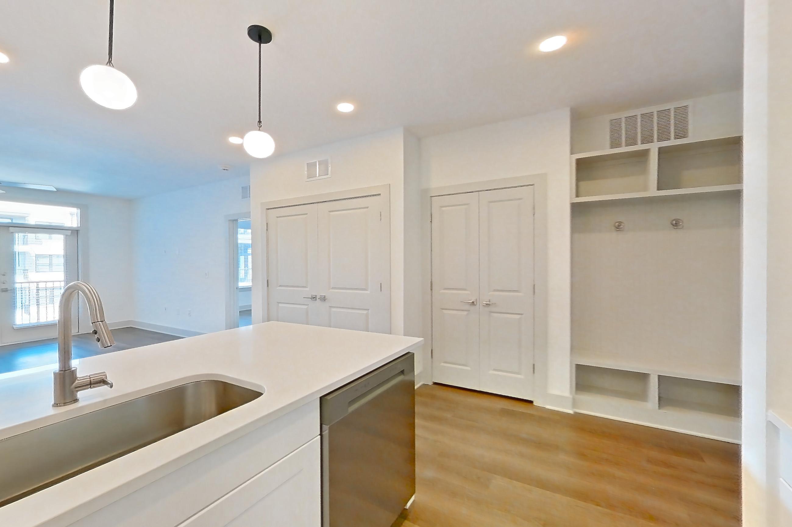 Kitchen with dark wood-finish flooring, dishwasher, electric range, kitchen island, light countertops, light stone countertops, light wood-finish flooring, oven/range, refrigerator, stainless steel appliances, and water & ice dispenser, Apartment 2352 at Groves South Congress