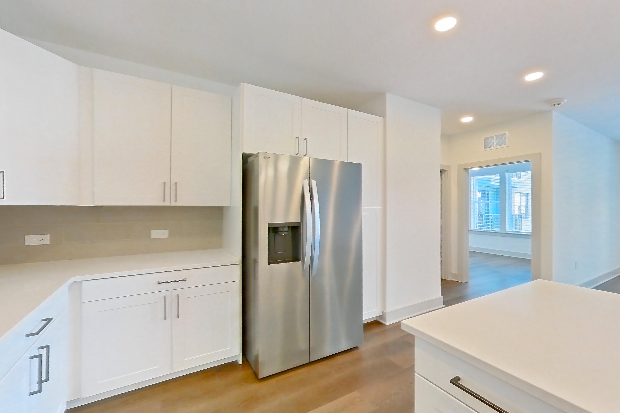 Kitchen with dark wood-finish flooring, dishwasher, electric range, kitchen island, light countertops, light stone countertops, light wood-finish flooring, oven/range, refrigerator, stainless steel appliances, and water & ice dispenser, Apartment 2352 at Groves South Congress