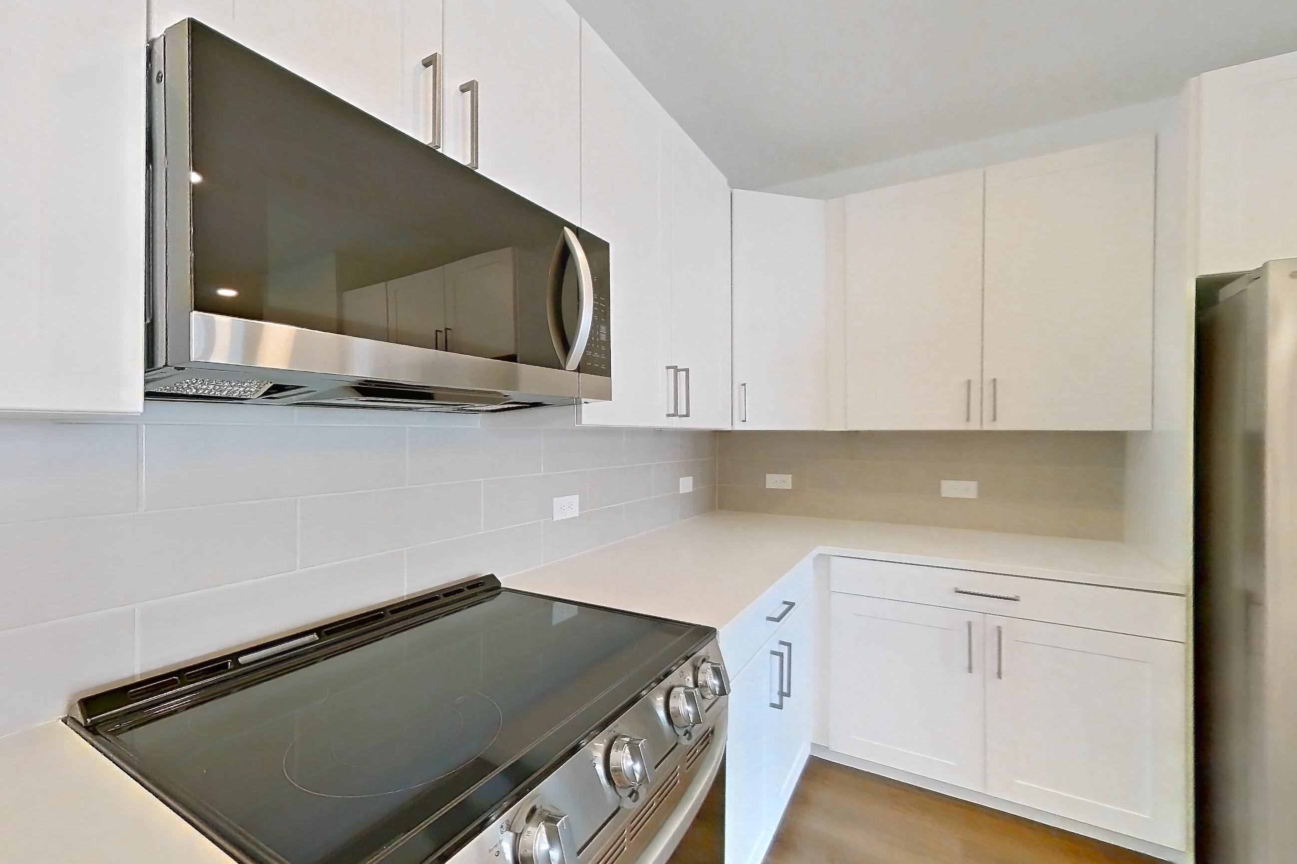 Kitchen with dark wood-finish flooring, dishwasher, electric range, kitchen island, light countertops, light stone countertops, light wood-finish flooring, oven/range, refrigerator, stainless steel appliances, and water & ice dispenser, Apartment 2352 at Groves South Congress