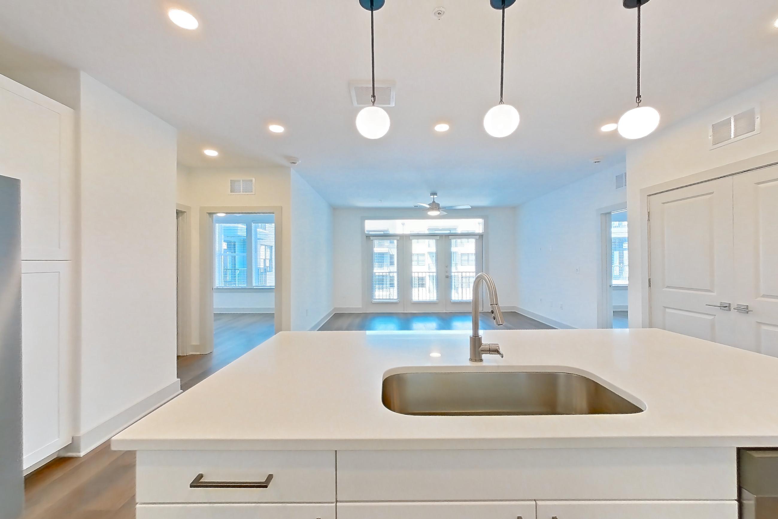 Kitchen with dark wood-finish flooring, dishwasher, electric range, kitchen island, light countertops, light stone countertops, light wood-finish flooring, oven/range, refrigerator, stainless steel appliances, and water & ice dispenser, Apartment 2352 at Groves South Congress