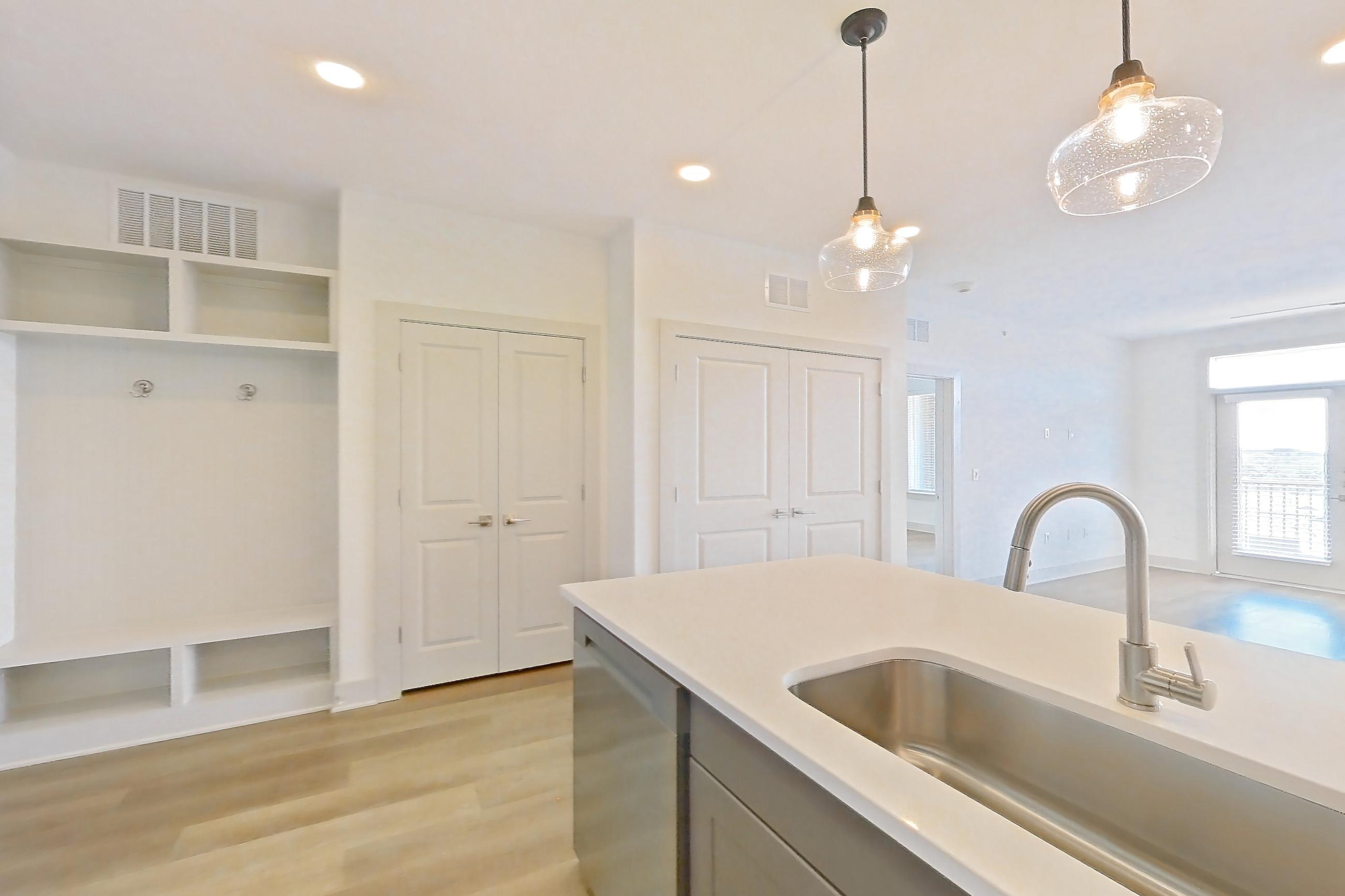 Kitchen with dishwasher, kitchen island, light countertops, light stone countertops, light wood-finish flooring, oven/range, refrigerator, stainless steel appliances, and water & ice dispenser, Apartment 2402 at Groves South Congress