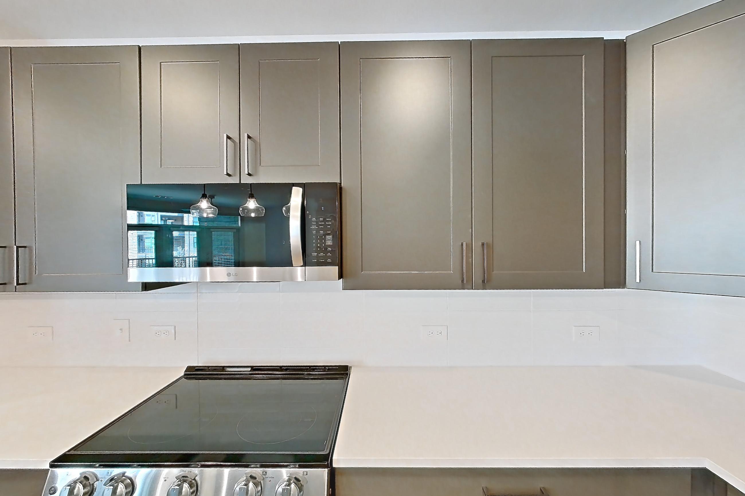 Kitchen with electric range, kitchen island, light countertops, light stone countertops, light wood-finish flooring, microwave, oven/range, range hood, refrigerator, stainless steel appliances, and water & ice dispenser, Apartment 2254 at Groves South Congress
