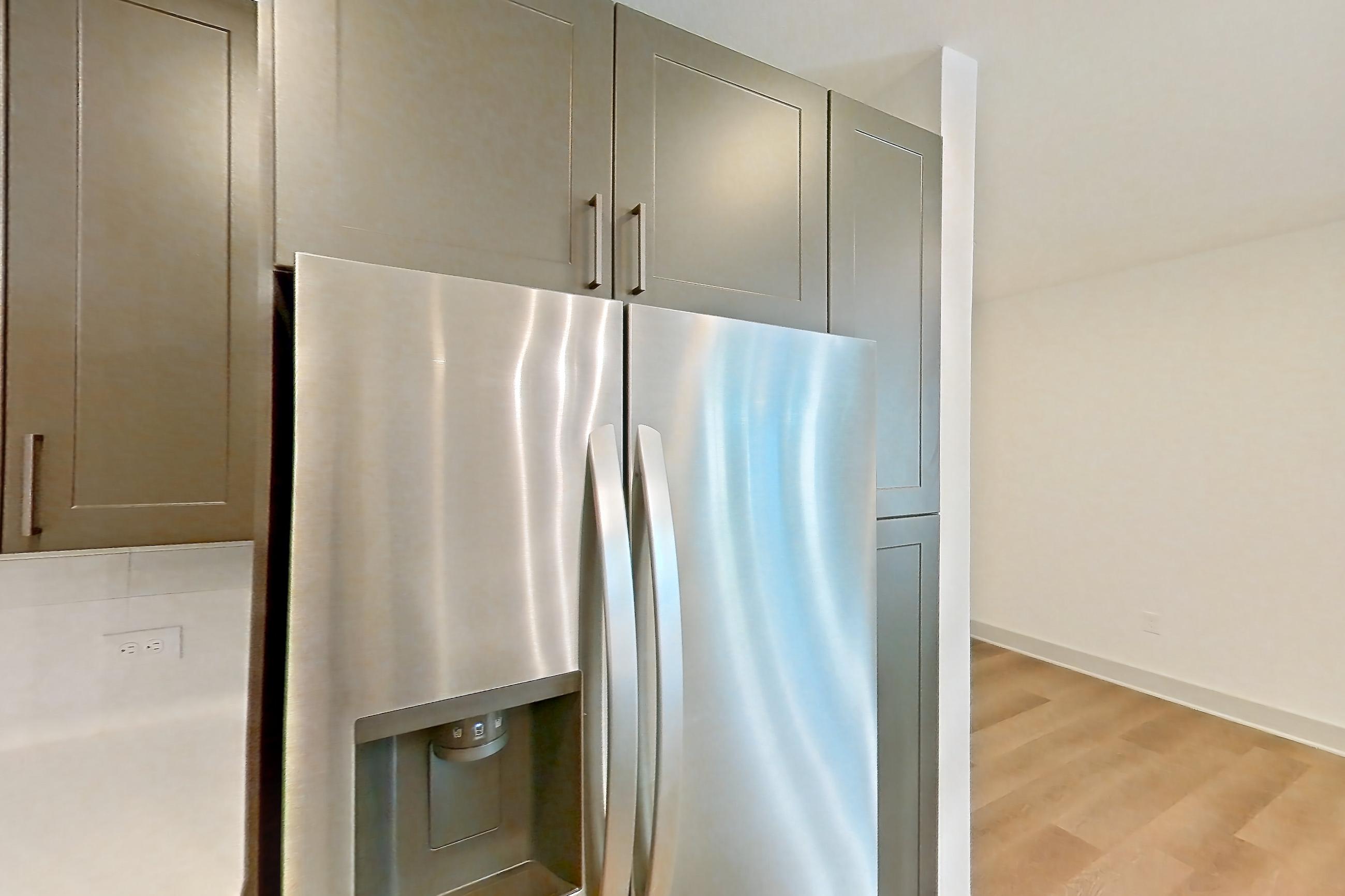 Kitchen with electric range, kitchen island, light countertops, light stone countertops, light wood-finish flooring, microwave, oven/range, range hood, refrigerator, stainless steel appliances, and water & ice dispenser, Apartment 2254 at Groves South Congress