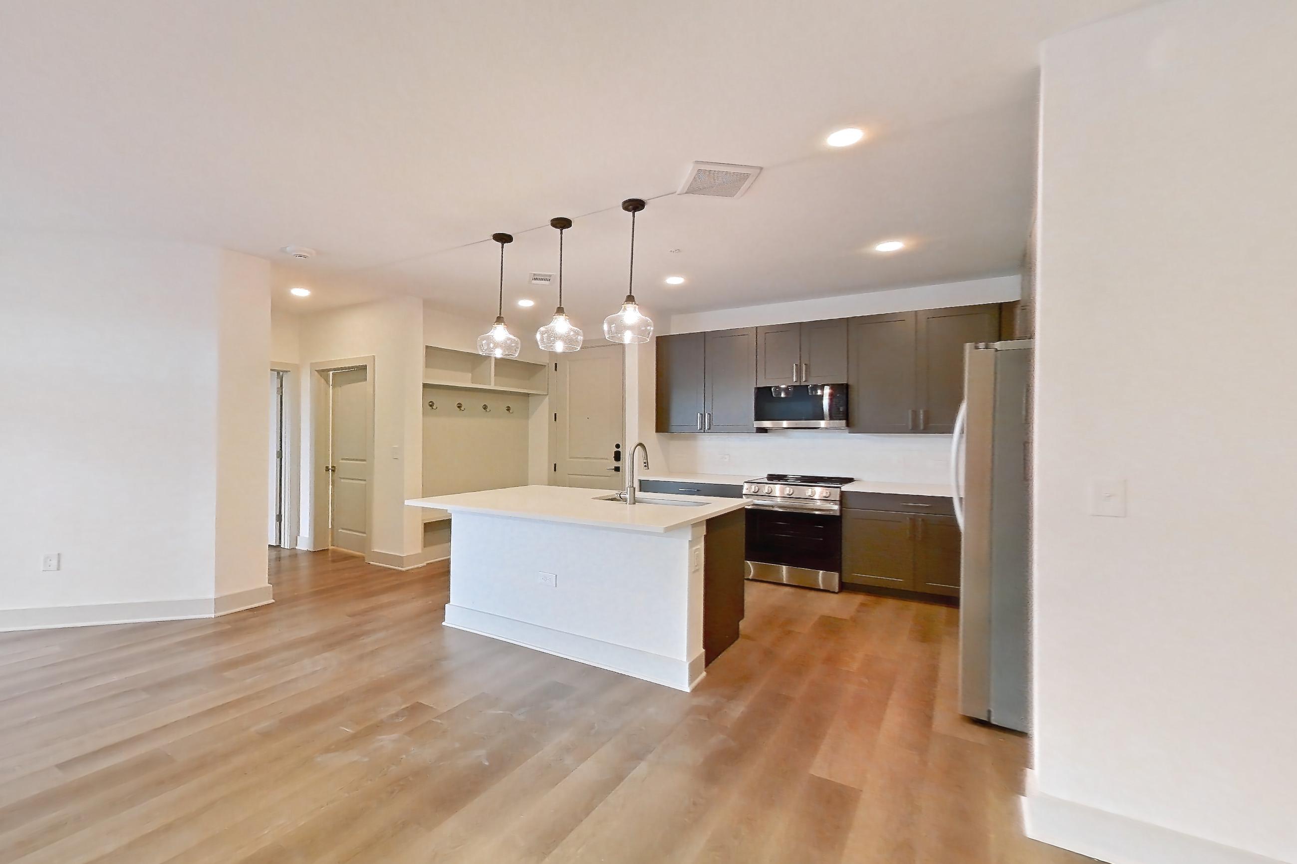Dining room with black appliances, electric range, kitchen island, light countertops, light wood-finish flooring, microwave, oven/range, refrigerator, stainless steel appliances, and white appliances, Apartment 2454 at Groves South Congress